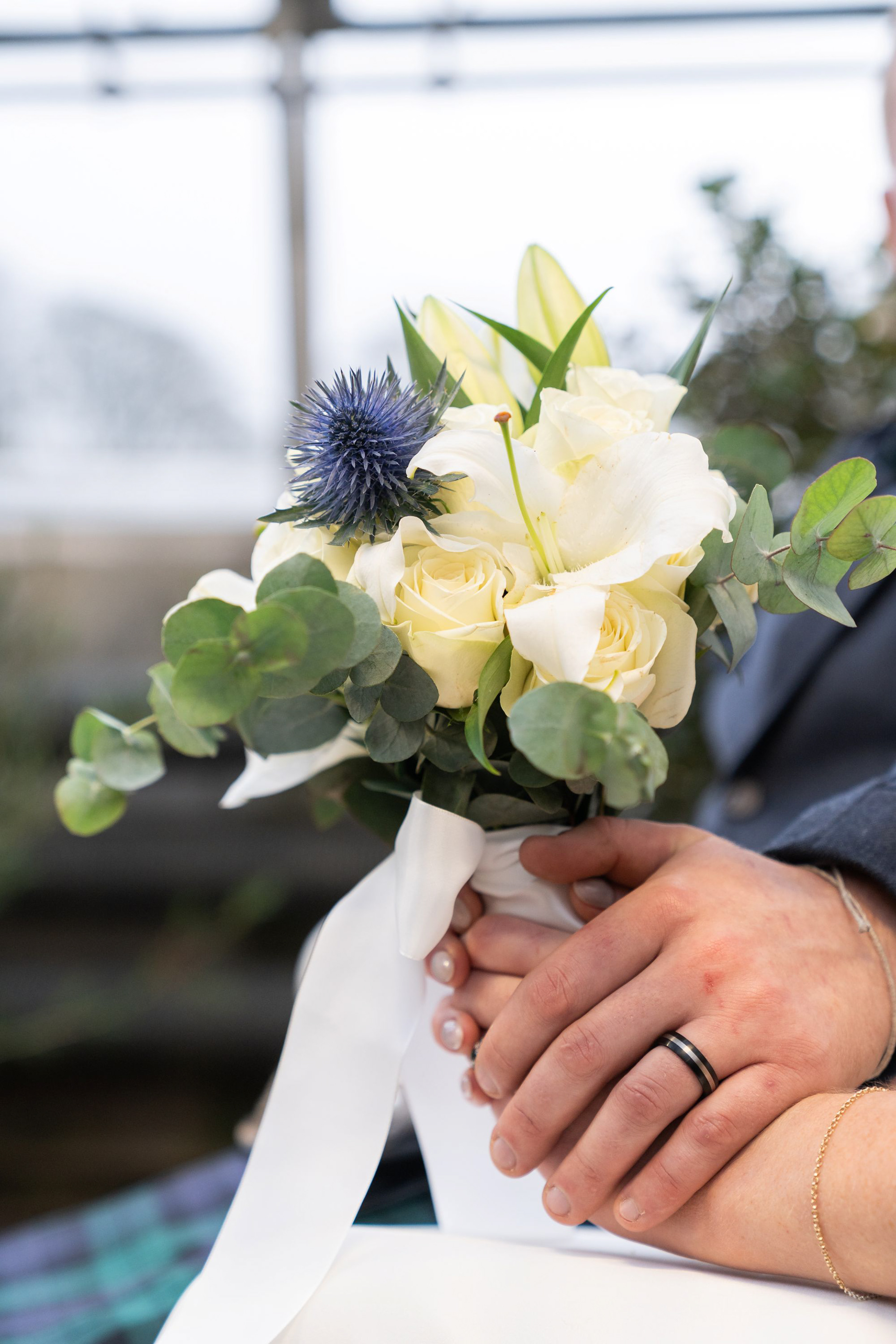 Detail shot of a bride and groom's hands holding a bouquet of cream and blue flowers.