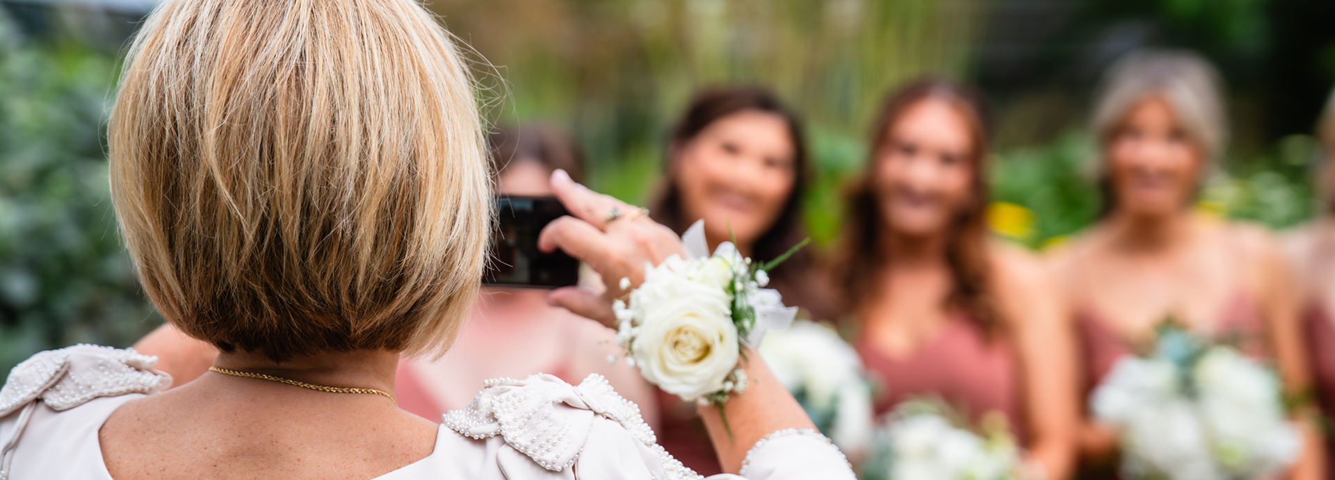 A short-haired woman with a corsage on her wrist takes a phone photo of several smiling bridesmaids at an Aberdeen Winter Gardens wedding.