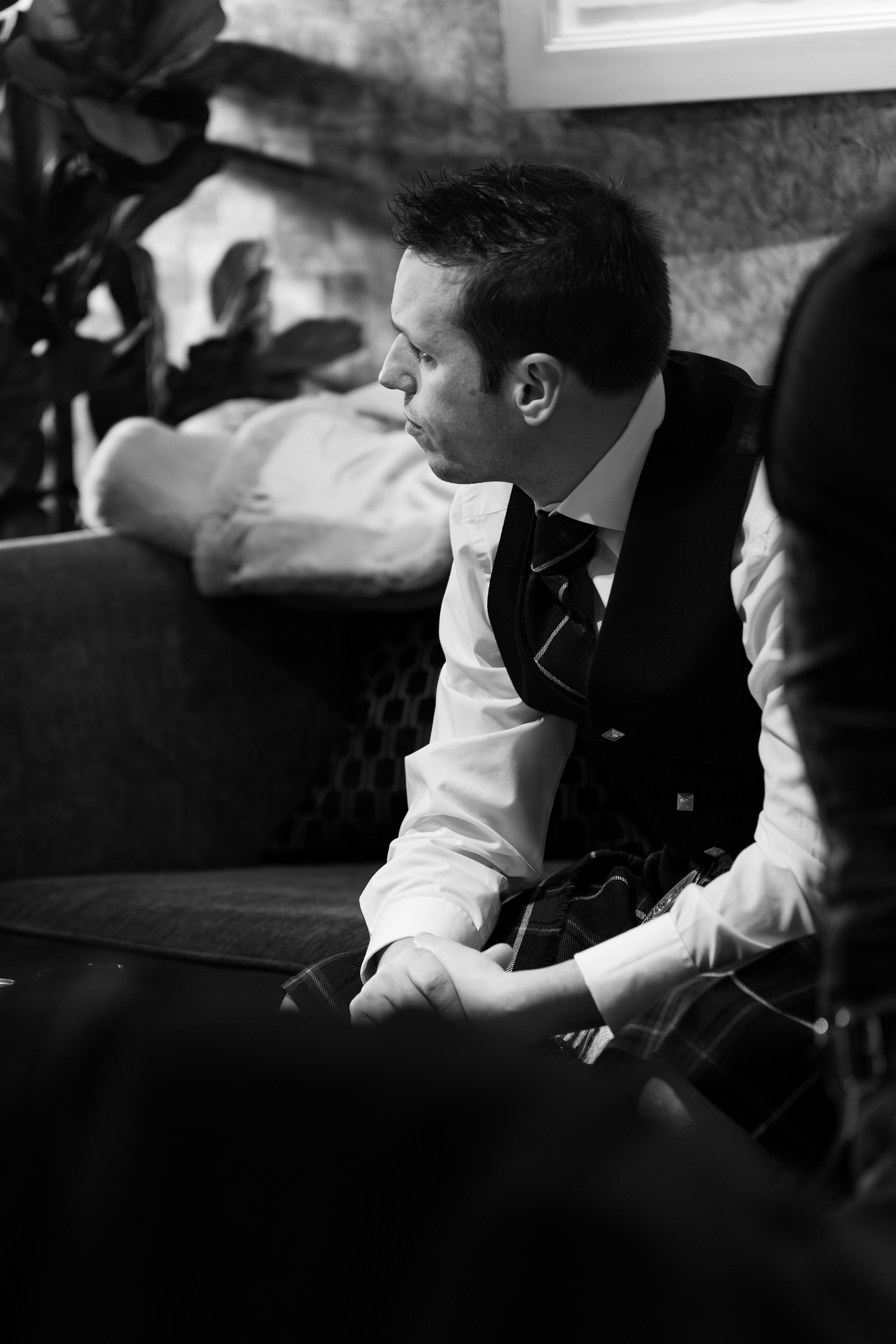 Wedding reception at Chester Hotel, Aberdeen: Black and white photo of a man in kilt sitting on a sofa, gazing off to one side.