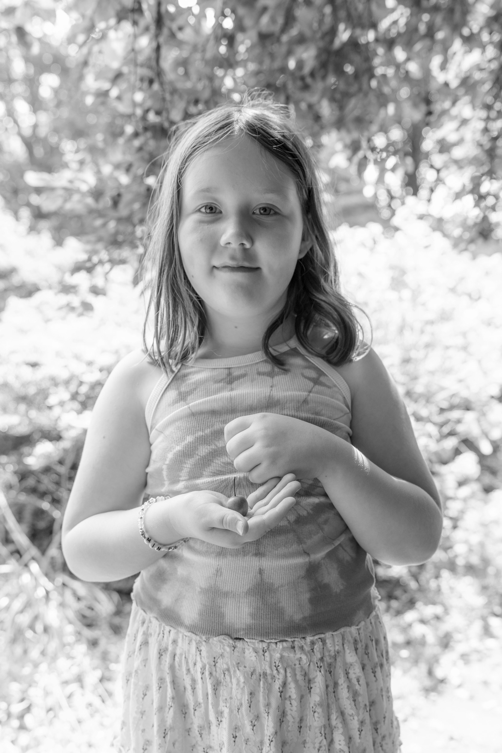 A 7 year old girl in a tie-dyed T-shirt stands, proudly cradling a small plum.