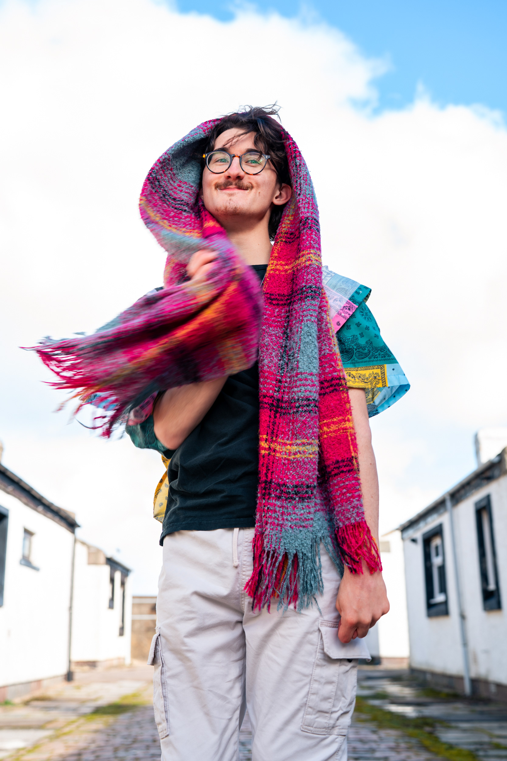 A man in glasses wraps a colourful scarf around his head and laughs.