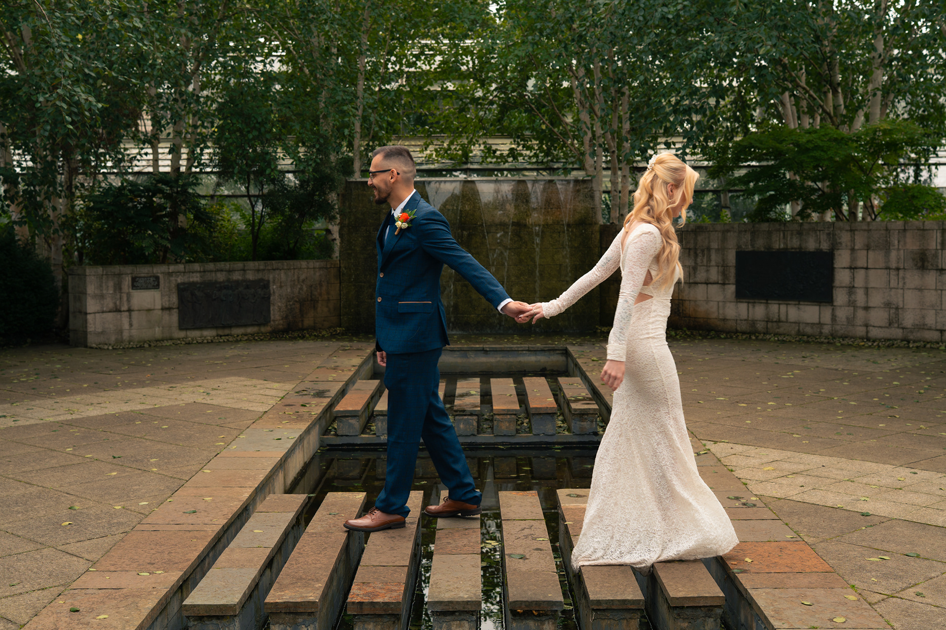 Duthie Park Winter Gardens wedding: Bride and groom touch hands as they pass on the stepping stones.