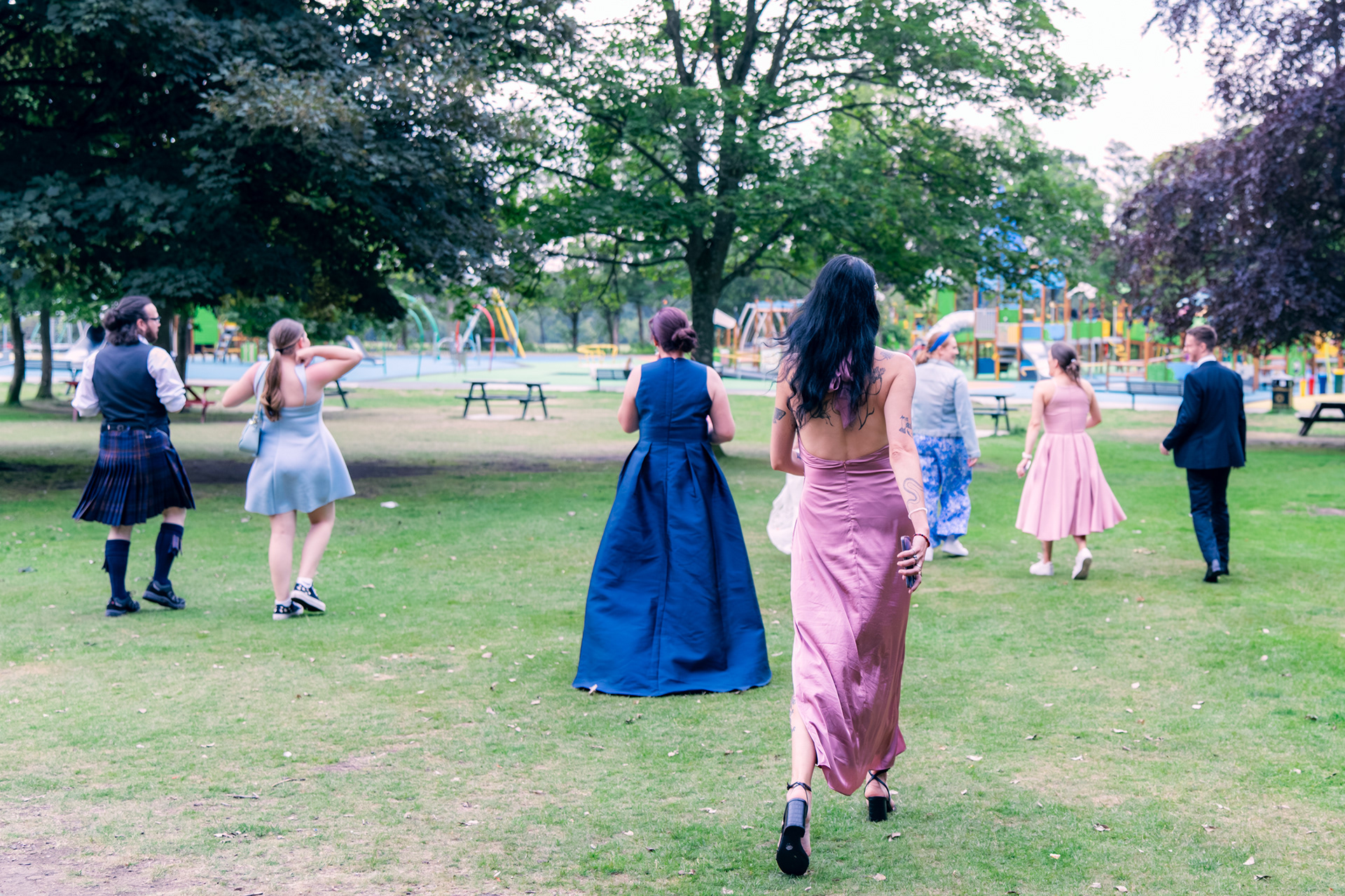 Wedding guests run across Hazlehead Park at dusk towards the swings