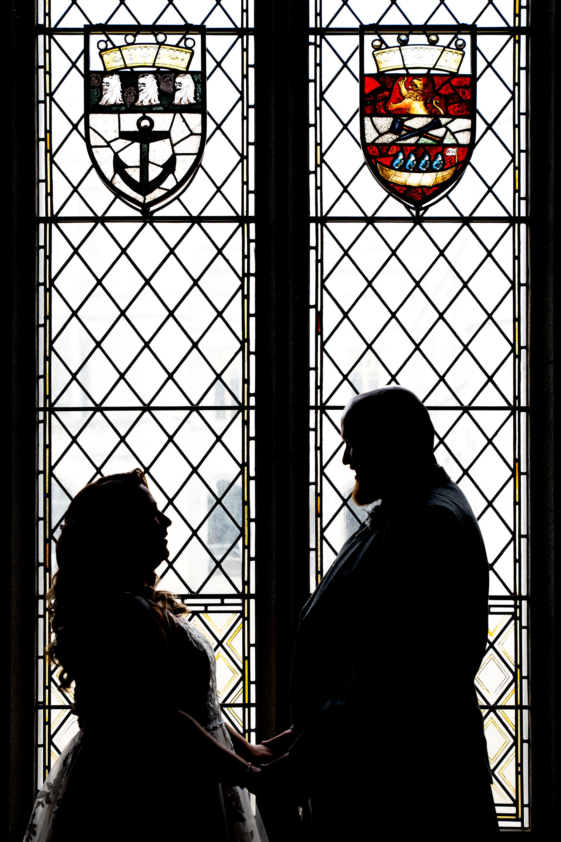 A bride and groom are silhouetted against a stained glass window in Aberdeen's Marischal College Grant Room. Wedding photography.