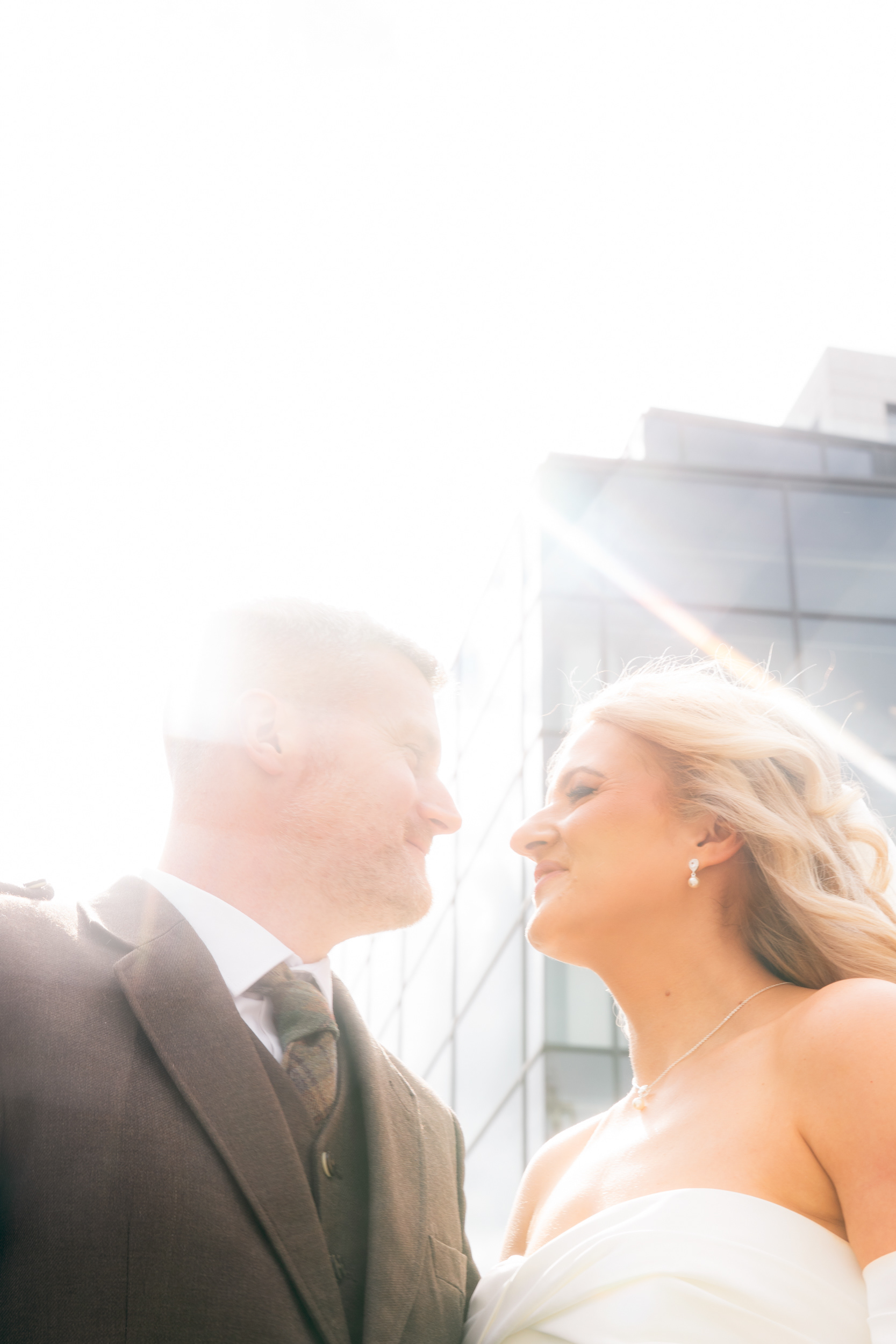Aberdeen registry office wedding: Bride and groom smile at each other as sunlight flares around them.