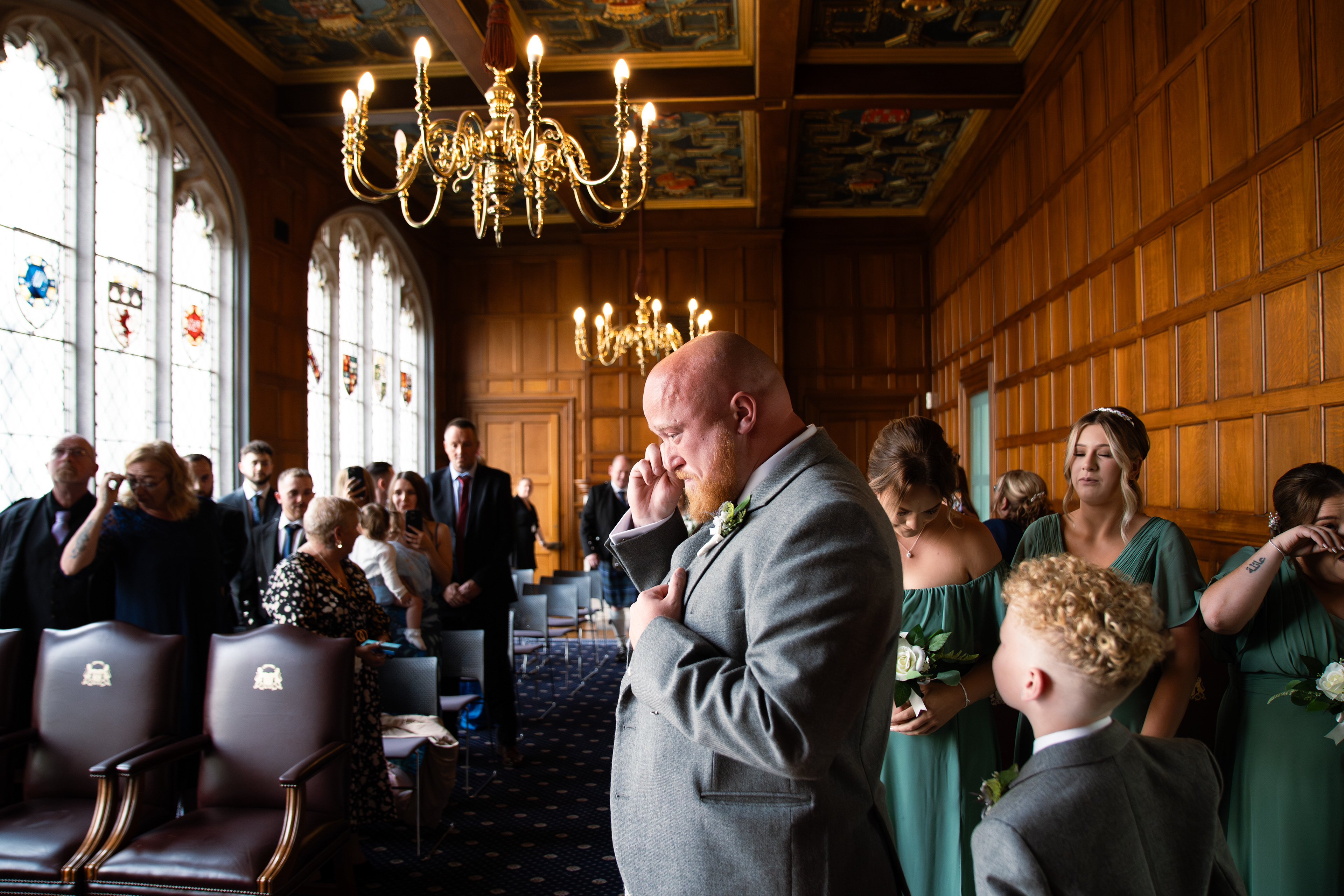 Groom in traditional Scottish kilt wipes tears from his eyes as his bride enters the ceremony room at Marischal College