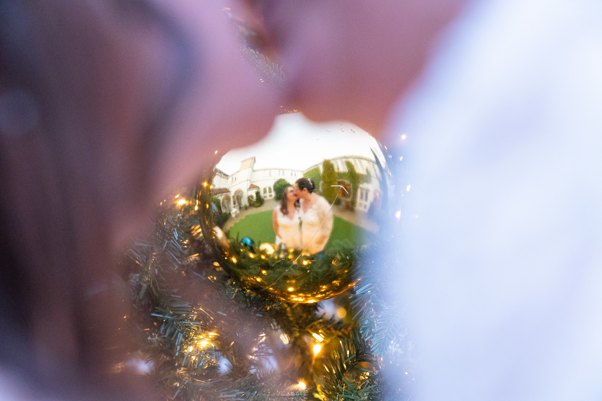 Two brides kissing are seen reflected in a large gold bauble on a Christmas tree. The Marcliffe is shown in the background.