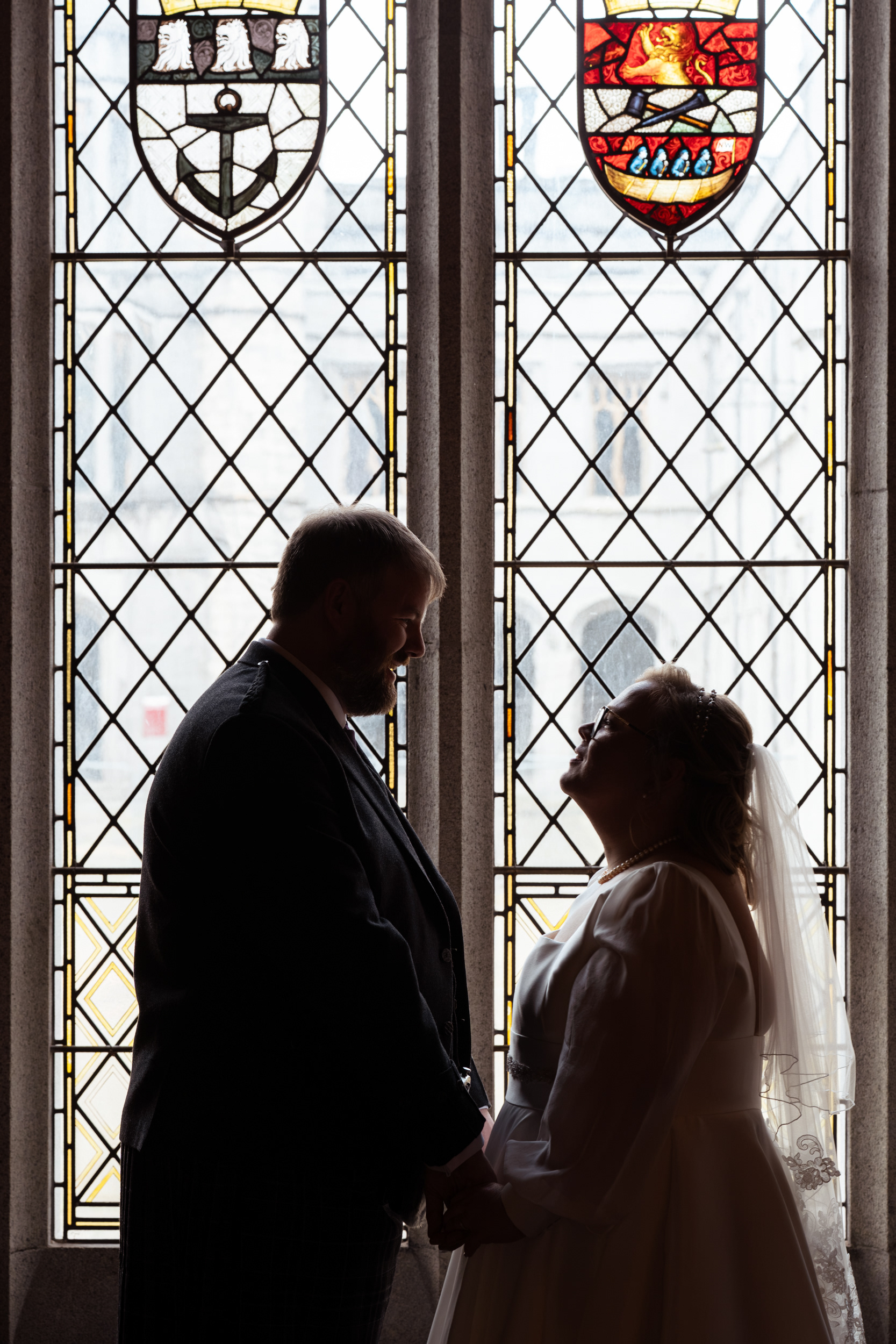 Aberdeen wedding photographer: Marischal College registry office wedding. Couple silhouetted against stained glass window.