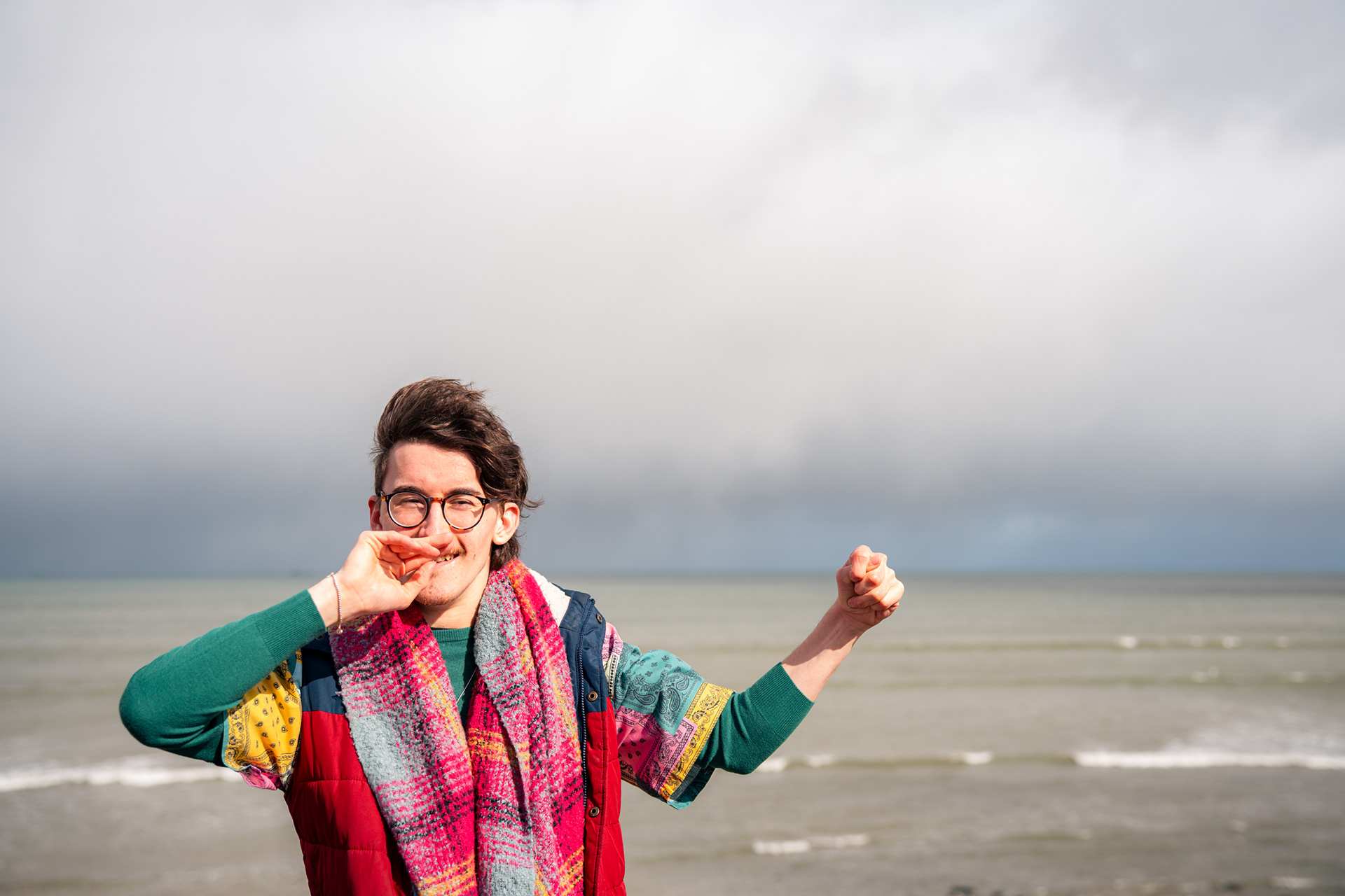 A young Disabled man laughs and looks to one side, the North Sea at Aberdeen Beach forming the backdrop.