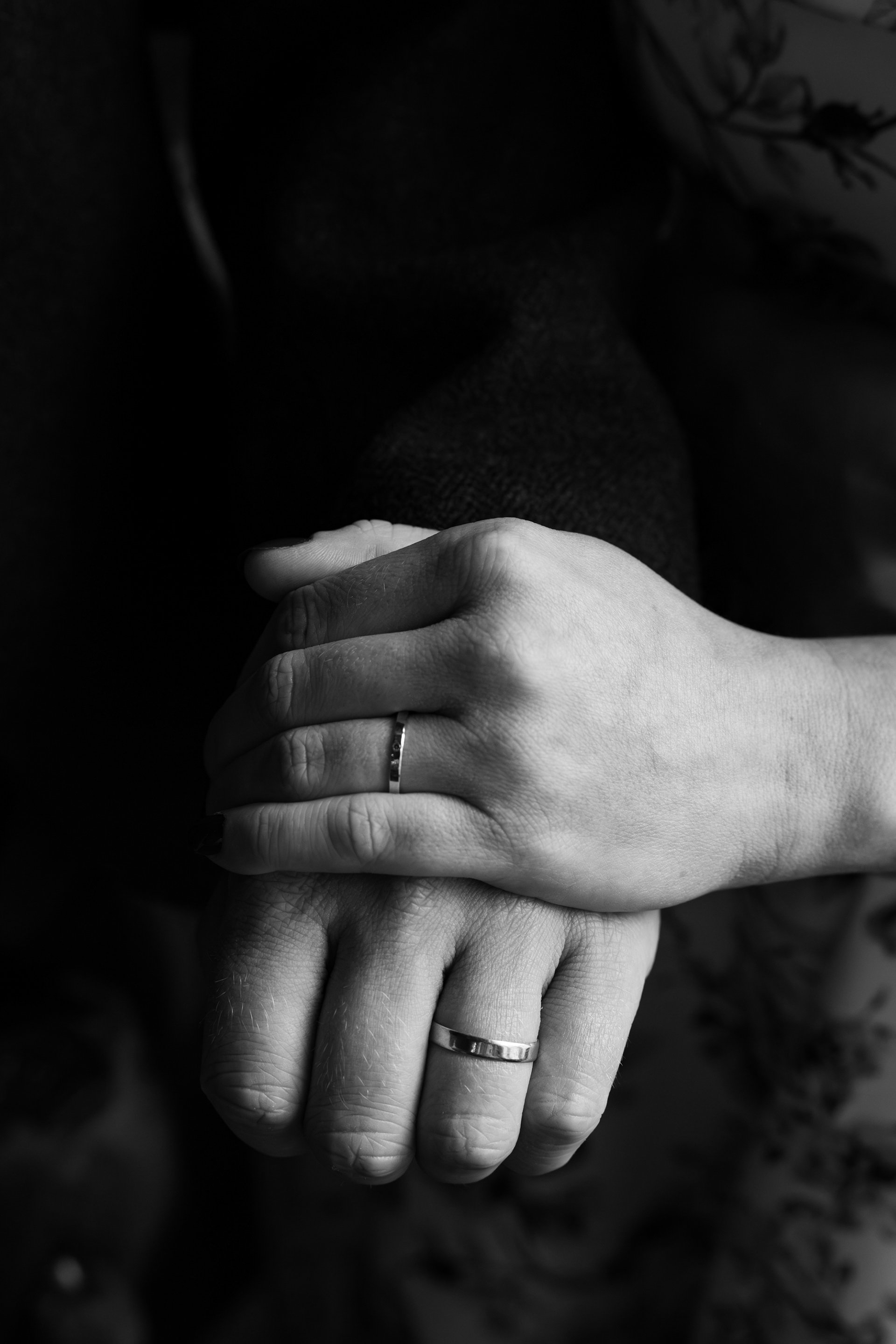 A black and white photo of a newlywed couple's hands, laid on top of each other, simply wedding bands visible.