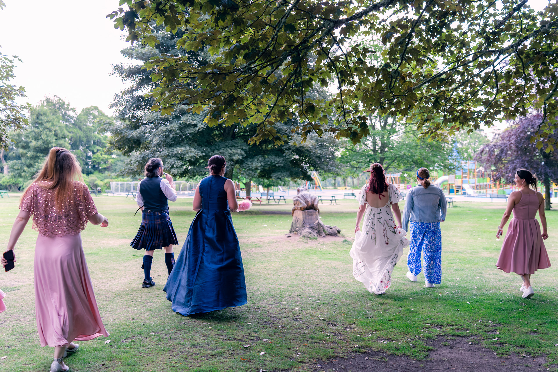 Wedding guests run across Hazlehead Park at dusk towards the swings