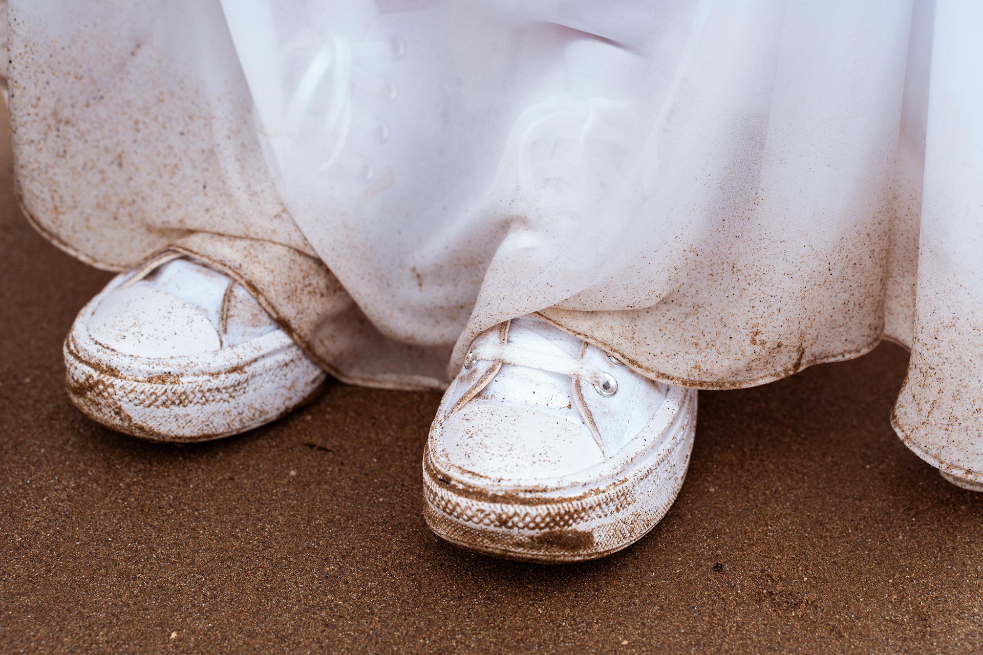Alternative Stonehaven elopement photographer: Close up of the bottom of the bride's white dress and white Converse, covered in wet sand, following a Scottish elopement.