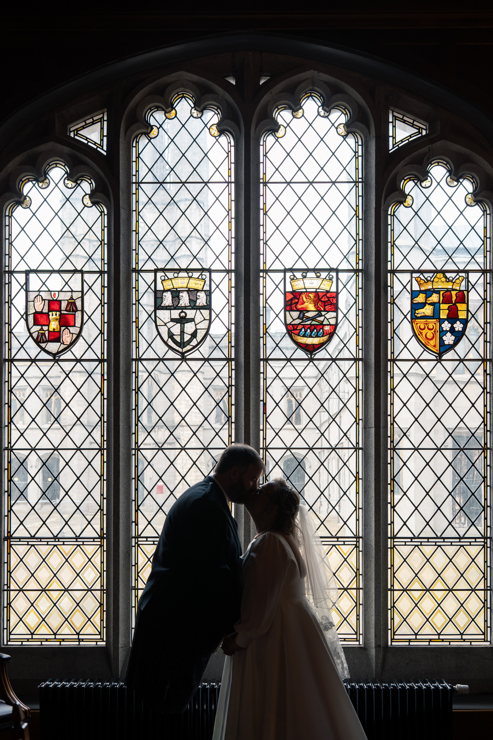 Bride and groom are silhouetted kissing in front of the stained glass window in Marischal College, Aberdeen