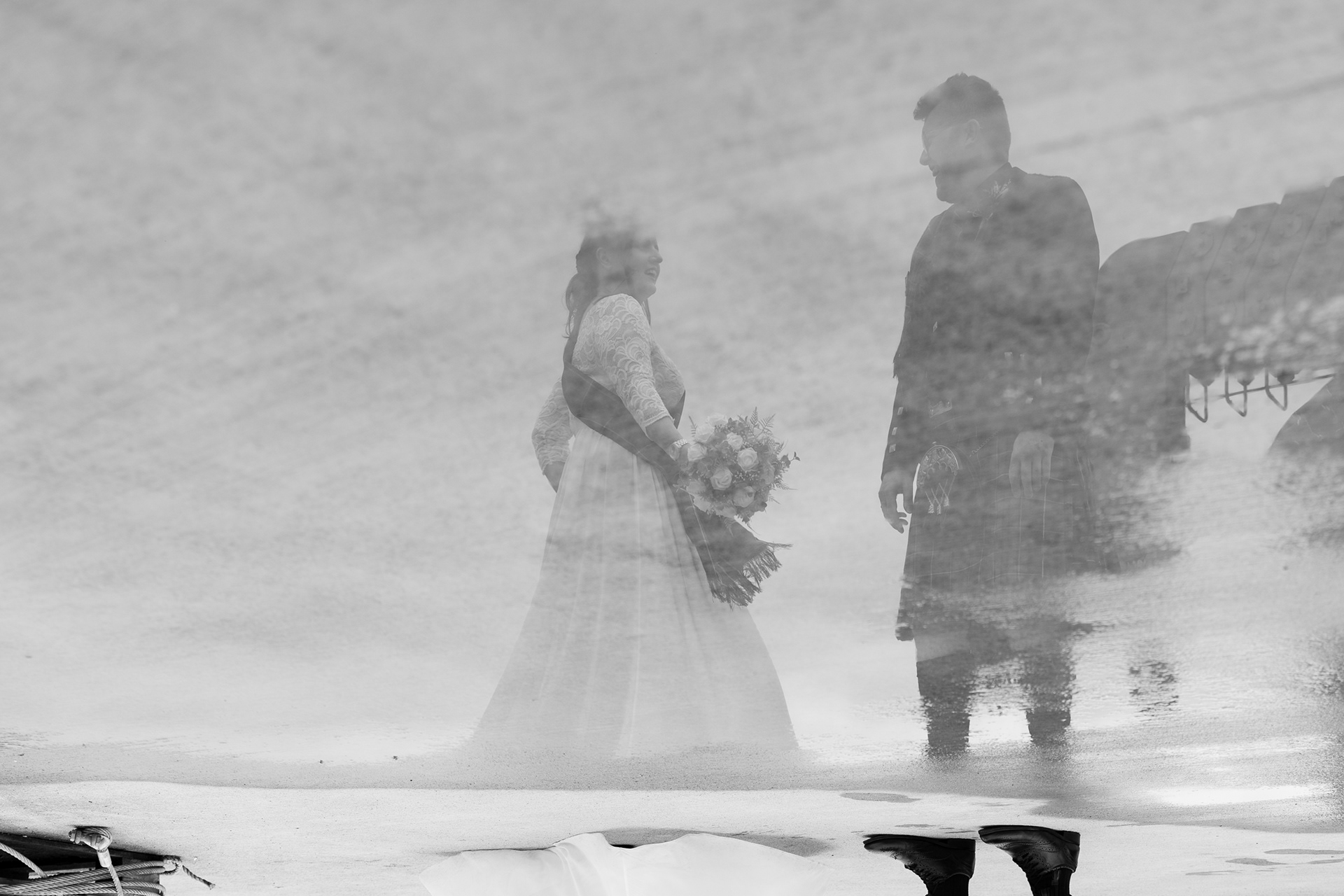 Alternative Aberdeenshire wedding photography: Bride and groom are shown laughing, reflected in a huge puddle, clear sky behind them, after their Stonehaven registry office wedding.