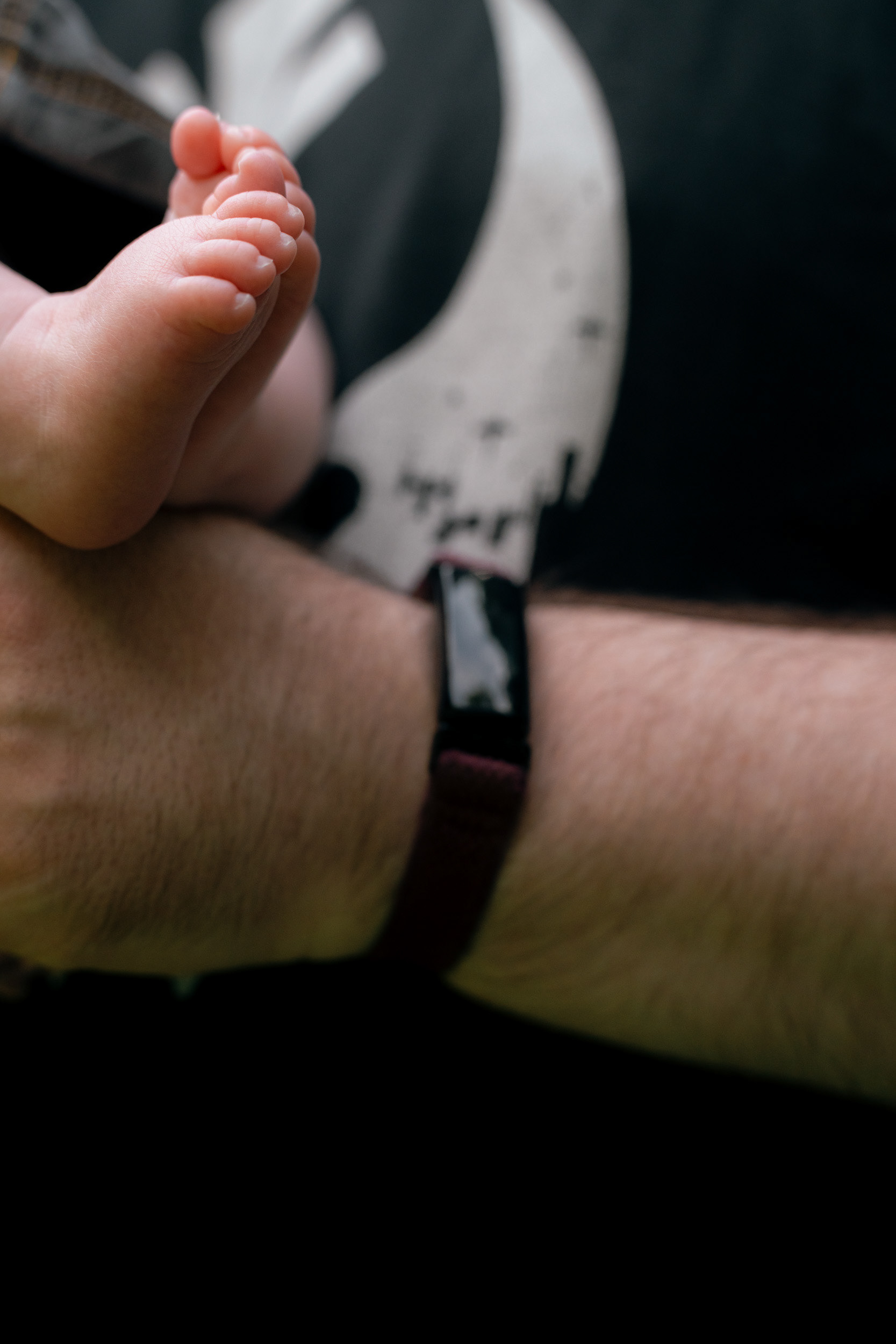 A close up of tiny newborn feet with teeny toes, resting on dad's much larger arm.