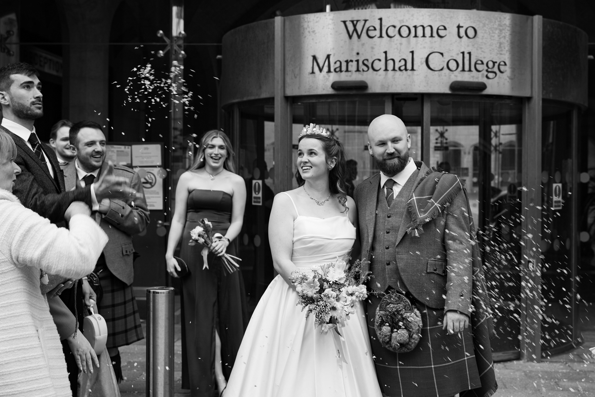 Newlyweds react with surprise as guests throw unexpected confetti at them outside Marischal College.