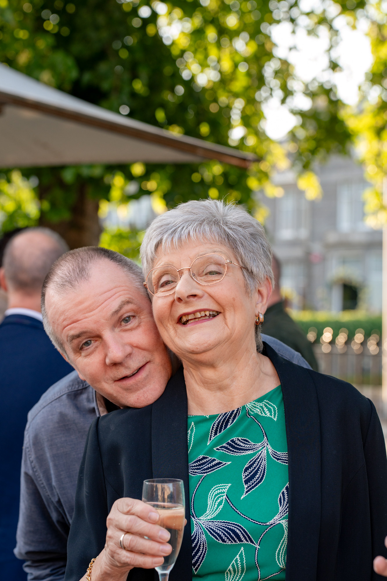 Aberdeen party photographer: A man in a grey suit pops his head over a woman in a green dress's shoulder as she smiles at the camera.