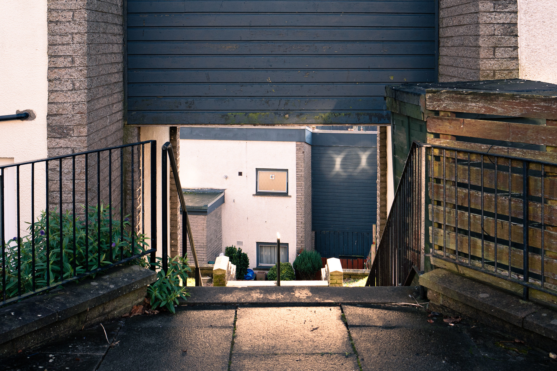 Looking down steep steps between the houses. At the bottom, sun from windows reflects onto another house.