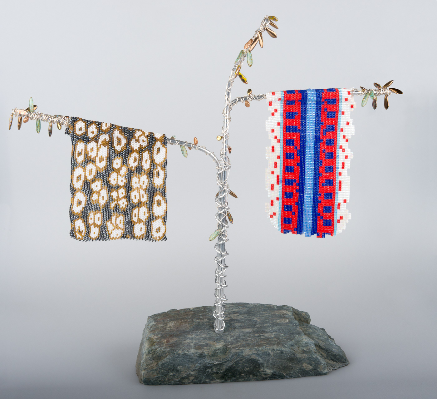 An island of Cumbrian Slate, supports an aluminium structure in the form of a dying tree. Beads represent dying leaves on the tree. From two of the branches hand the skins of two endangered animals created in hand woven Miyuki beads. One is the highly coloured California red sided garter snake, and the other is the Coachella fringe toed lizard