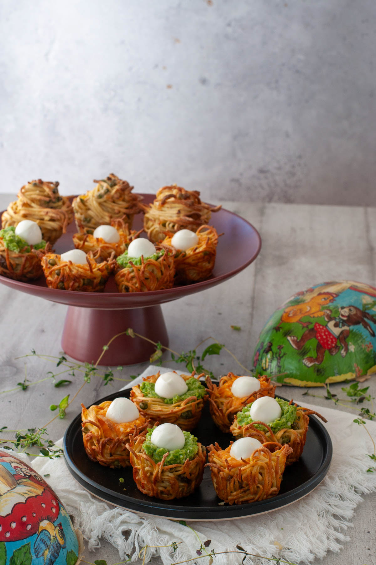 Nidi di pasta al forno con ripieni colorati e mozzarelline su alzata rossa e uova di Pasqua d'epoca.