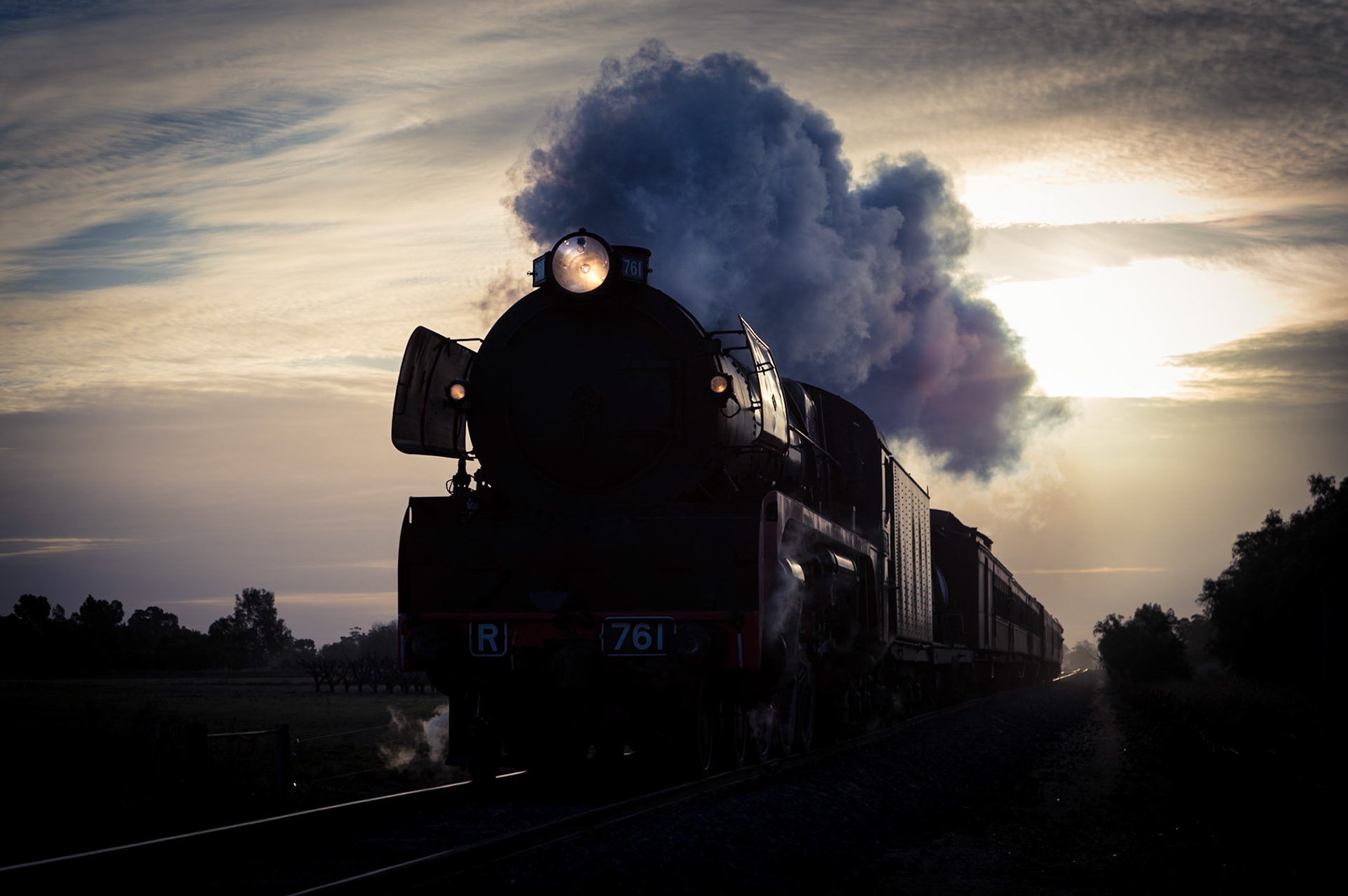 On the outskirts of Kyabram in northern Victoria, R761 glides along golden rails, with the winter sunset as a backdrop. R761 and its train are captured returning from Echuca via Toolamba, with Steamrail's Echuca Explorer train. The Toolamba-Echuca section is rarely used by passengers, as most Echuca trains run via Bendigo.