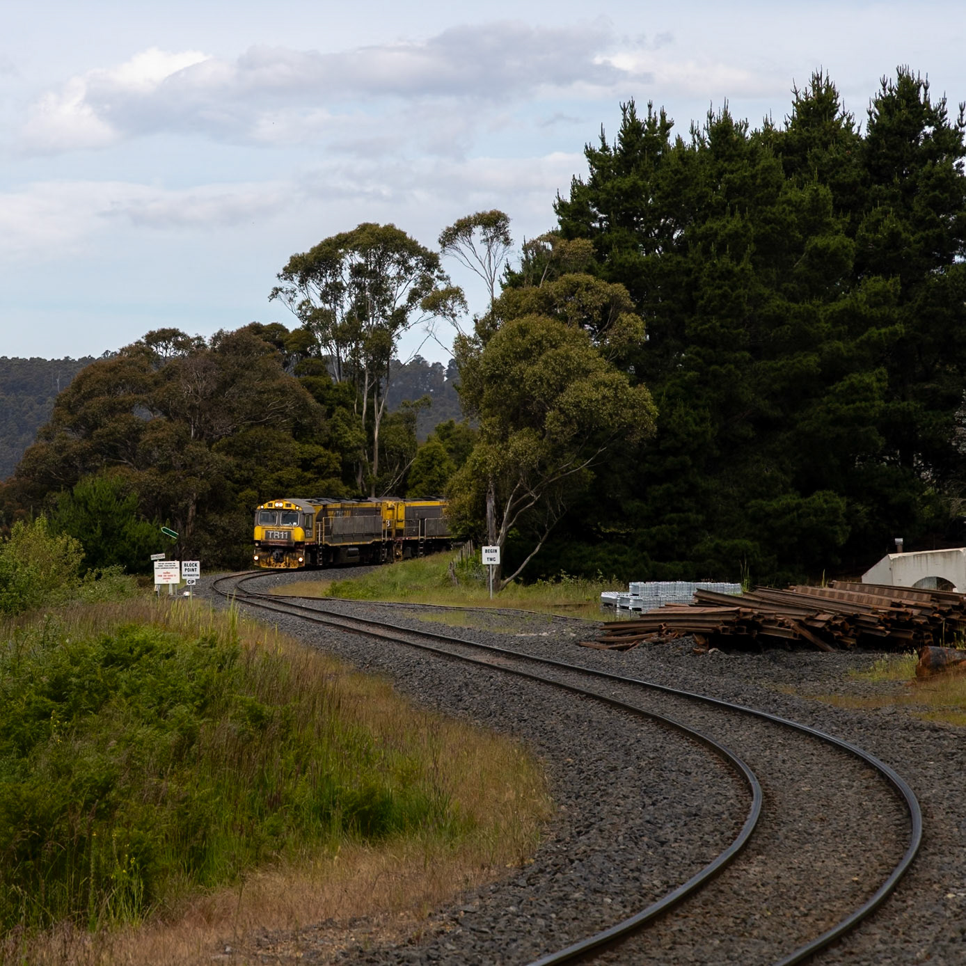 TR11 and TR13 roll through Rhyndaston with a train from Boyer to Burne. The quiet country town has taken on the role of way and works depot, with steel sleepers, track, and concrete culverts all deposited ready for the next round of permanent way upgrades.
