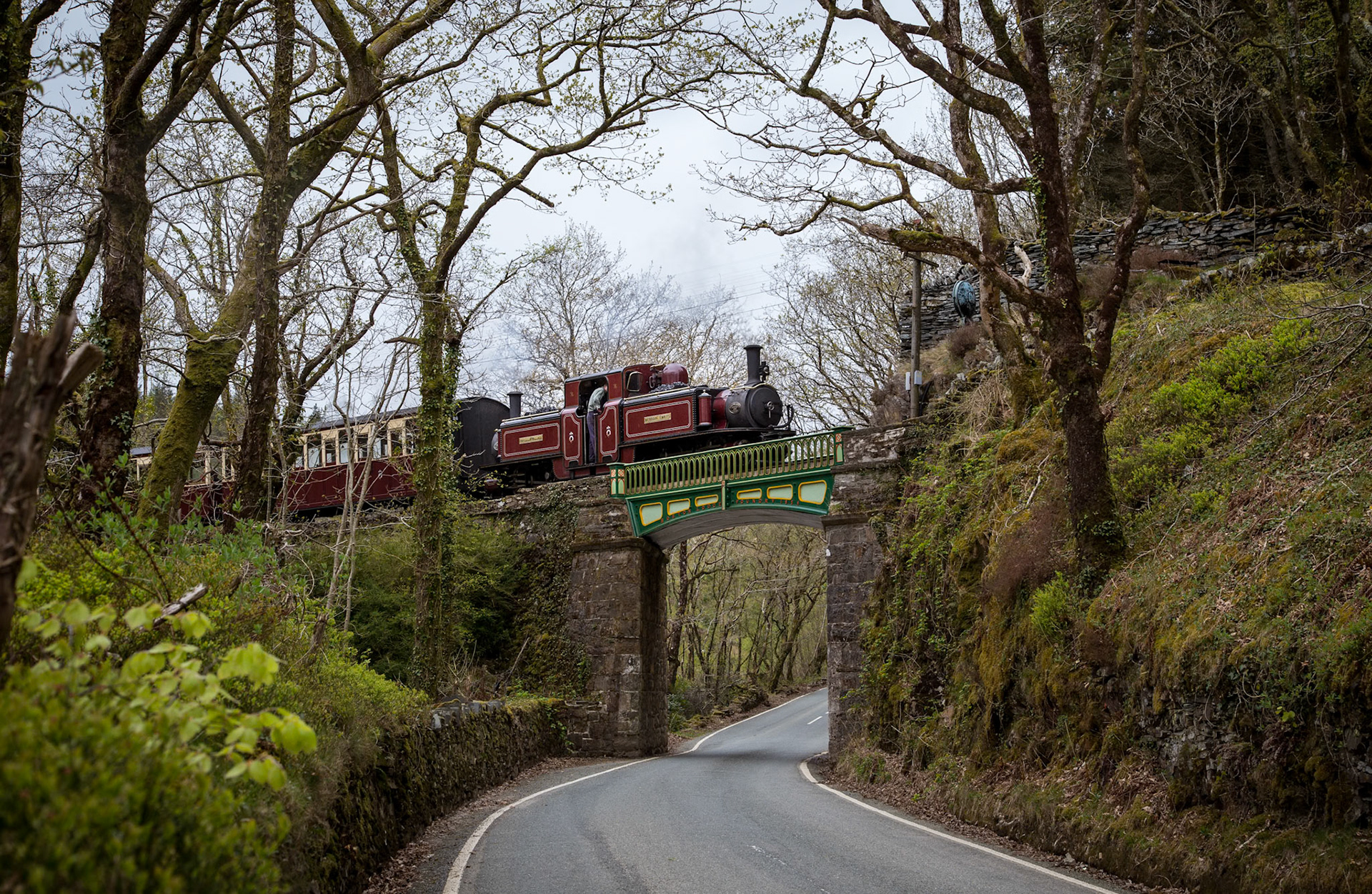 Amongst the trees and moss, one of the Ffestiniog Railway's iconic double-Fairlie locomotives, Merddin Emrys, crosses the iron bridge immediately before Tan-y-Bwlch station with a train from Porthmadog to Blaenau Ffestiniog. The iron bridge was built by the railway's workshops in 1854 - the same workshops that continue to manufacture new carriages and locomotives for the booming tourist railway.