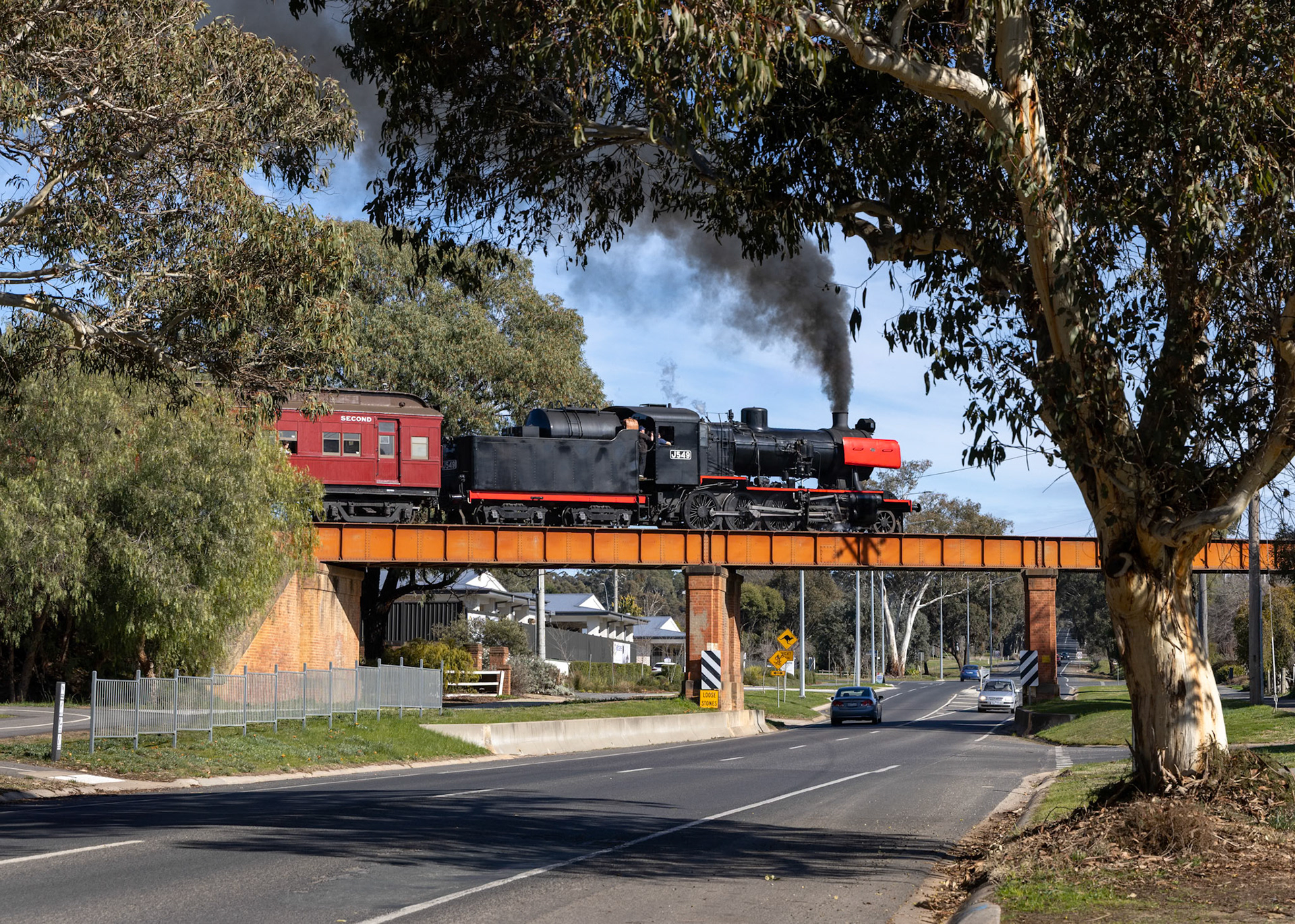 On the outskirts of Castlemaine, J549 crosses over the Pyrenees Highway with the 10:45 departure for Maldon.The morning sunlight highlights the distinctive SCOA-P driving wheels; developed by the Steel Company of Australia as part of the R class development in the late 1940s, these used U-shaped spokes to strengthen the wheel without adding excessive weight.