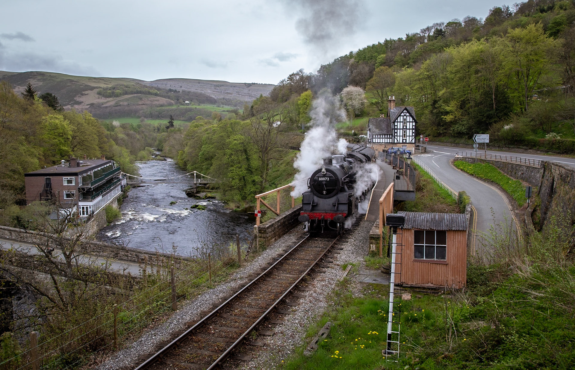Hugging the valley formed by the River Dee, the picturesque station of Berwyn extends its platform along the railway viaduct which in turn spans a road viaduct. This site is famous for the Berwyn chain bridge, one of the earliest crossings of the fast flowing River Dee. Situated on the present day Llangollen Railway the station was opened in 1865 as part of the Llangollen and Corwen railway, which later formed part of the larger Ruabon-Barmouth railway. The station fell into disuse in December 1964, before the lines closure in January 1965.