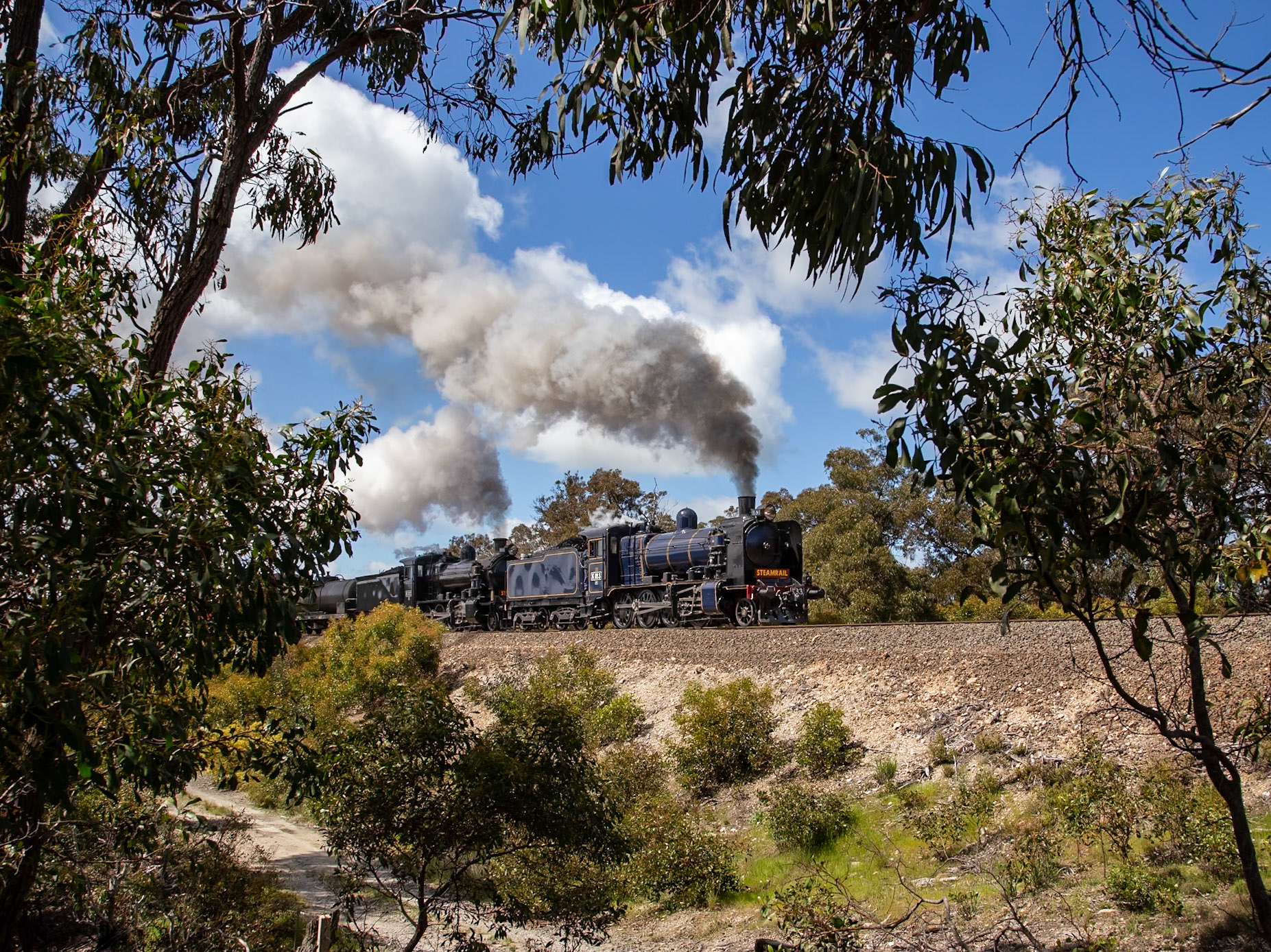 Resplendent in its iconic blue and gold livery, K183 leads K153 (masquerading as class leader K100) through the lush bush landscape of Ironbark Gorge with a "Triple Ks" special from Melbourne to Ballarat. Absent from the scheduled triple-header is K190, which suffered a last-minute boiler defect as the train was being assembled that morning.