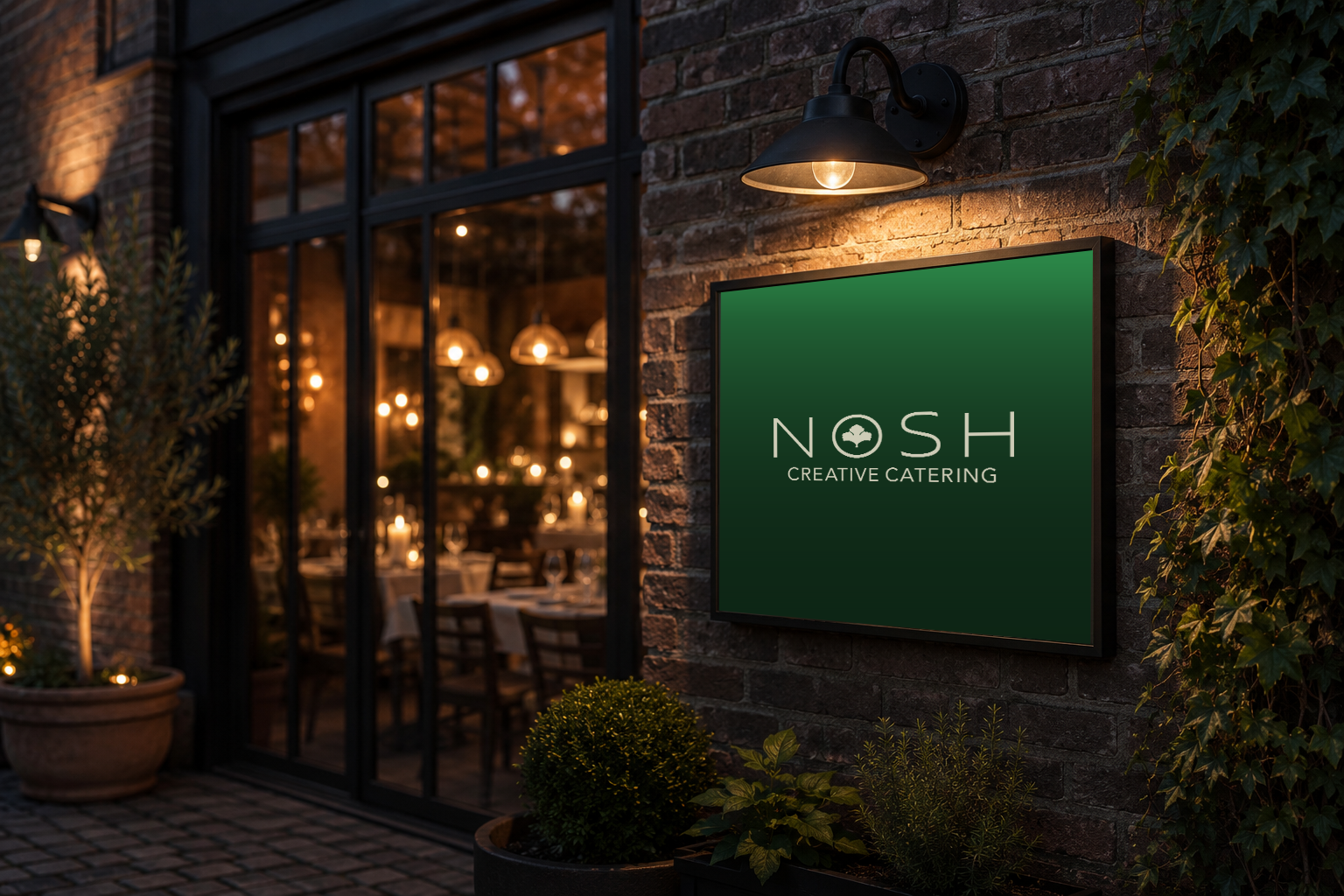Evening restaurant exterior with an illuminated green Nosh Creative Catering sign.