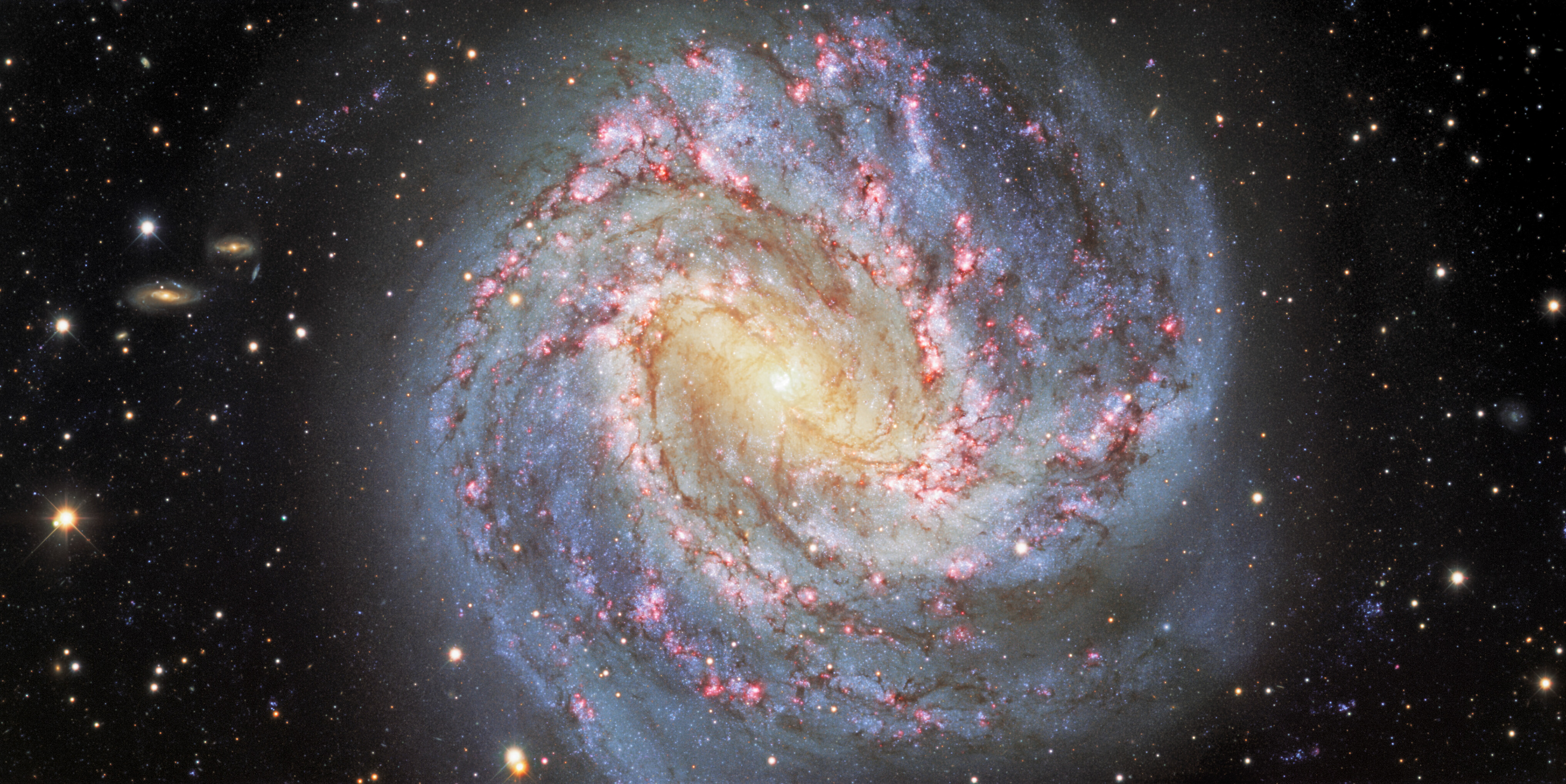 Nicknamed the Southern Pinwheel, Messier 83 (or NGC 5236) is a stunning face-on spiral galaxy located about 15 million light-years away in the southern constellation of Hydra. Its spiral arms are lined with dark lanes of dust and peppered with reddish, star-forming clouds of hydrogen gas. One of the deepest images ever taken of the Southern Pinwheel (combining more than 11 hours of exposure time), this view was captured with the Dark Energy Camera (DECam), which was built by the US Department of Energy (DOE) and is mounted on the Víctor M. Blanco 4-meter Telescope at Cerro Tololo Inter-American Observatory (CTIO), a Program of NSF’s NOIRLab. Numerous background galaxies, which lie much farther away than Messier 83, appear around the edges of the image.  Credit: CTIO/NOIRLab/DOE/NSF/AURA Acknowledgment: M. Soraisam (University of Illinois) Image processing: Travis Rector (University of Alaska Anchorage), Mahdi Zamani & Davide de Martin