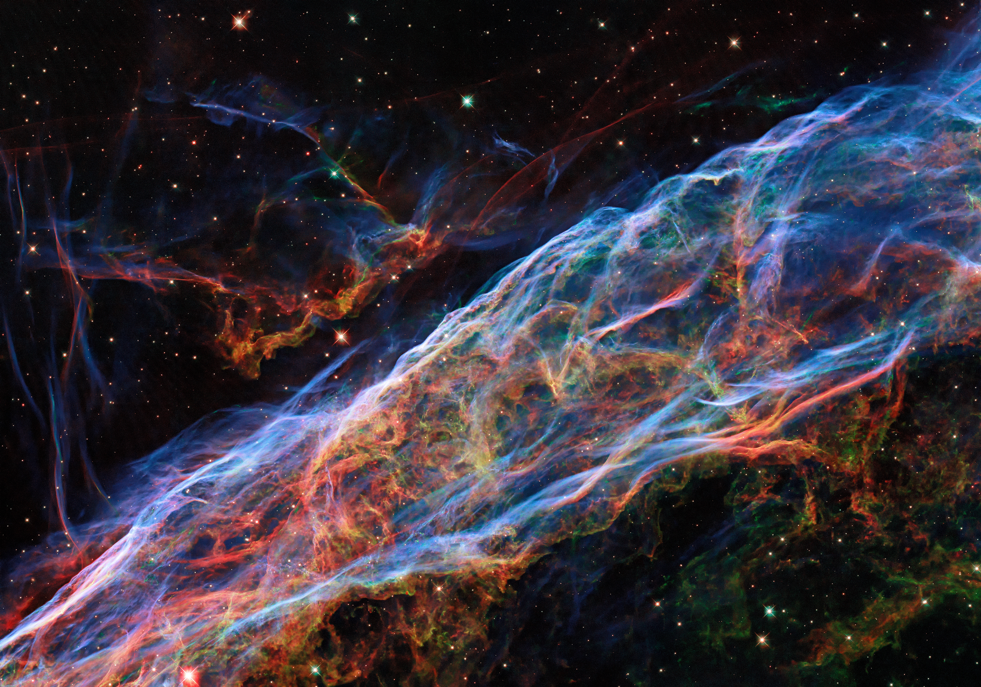 This Picture of the Week revisits the Veil Nebula, a popular subject for Hubble images! This object was featured in a previous Hubble photo release, but now new processing techniques have been applied, bringing out fine details of the nebula’s delicate threads and filaments of ionised gas.  To create this colourful image, observations taken by Hubble's Wide Field Camera 3 instrument through 5 different filters were used. The new post-processing methods have further enhanced details of emissions from doubly ionised oxygen (seen here in blues), ionised hydrogen and ionised nitrogen (seen here in reds).  The Veil Nebula lies around 2100 light-years from Earth in the constellation of Cygnus (The Swan), making it a relatively close neighbour in astronomical terms. Only a small portion of the nebula was captured in this image.  The Veil Nebula is the visible portion of the nearby Cygnus Loop, a supernova remnant formed roughly 10 000 years ago by the death of a massive star. The Veil Nebula’s progenitor star — which was 20 times the mass of the Sun — lived fast and died young, ending its life in a cataclysmic release of energy. Despite this stellar violence, the shockwaves and debris from the supernova sculpted the Veil Nebula’s delicate tracery of ionised gas — creating a scene of surprising astronomical beauty.  Credit: ESA/Hubble & NASA, Z. Levay