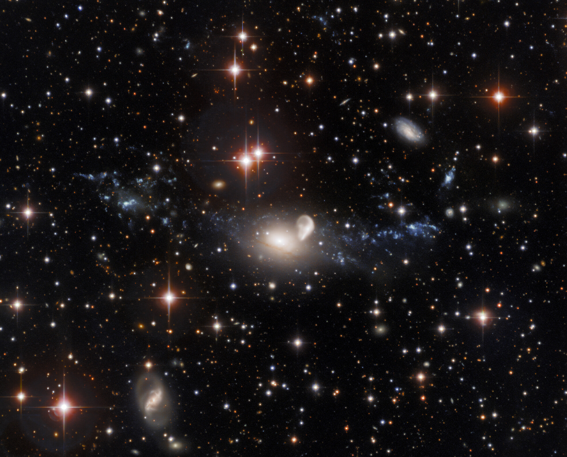 This observation from the SMARTS 0.9-meter Telescope at Cerro Tololo Inter-American Observatory shows the result of a truly spectacular galactic collision. The elliptical galaxy NGC 5291 — the hazy oval cloud at the center of this image — was struck by a careening rogue galaxy over 300 million years ago. The aftermath of this cataclysmic collision is a ring of galactic debris — visible as the tenuous luminous clouds spreading left and right from the golden oval of NGC 5291. This image also shows more gentle galactic interactions — NGC 5291 is interacting sedately with the unusually curved galaxy to the right of it, which is known as the Seashell.  Credit: CTIO/NOIRLab/NSF/AURA  Acknowledgments: Travis Rector (University of Alaska Anchorage), Mahdi Zamani & Davide de Martin