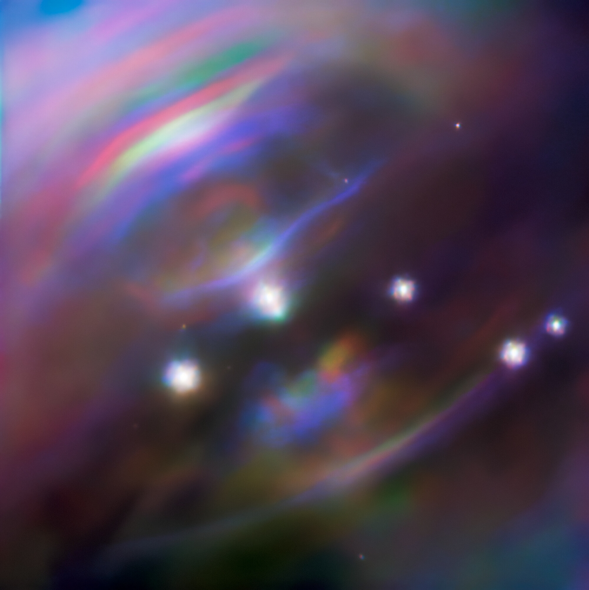 In the heart of the Crab Nebula (Messier 1) a neutron star is rotating 30 times every single second. This pirouetting star, known as the Crab Pulsar, consists purely of neutrons, and has an intense magnetic field which ejects jets of material from its poles at nearly the speed of light. The Crab Pulsar has a mass about one and a half times that of our Sun, yet all this mass is packed into a sphere only 28 km (17 miles) in diameter — roughly the size of Mars’s small moon Phobos.  The wispy structures shown in this image are caused by material flowing equatorially outwards from the pulsar and careening into the surrounding nebula. These dynamic features, known as termination shocks, move and change shape as outflow from the puslar ebbs and flows.   This changeability is showcased by this composite image, which is a compilation of three Gemini North observations taken over a 5-year period at the same infrared wavelength: observations from October 2009 are shown in blue and observations from December 2014 are shown in red. This color coding of the observations produces a striking rainbow effect highlighting the high speed motion of the termination shocks, which have noticeably changed position between observations. Gemini North on Maunakea, Hawai‘i, is one of the pair of telescopes that make up the international Gemini Observatory, a Program of NSF’s NOIRLab.  Credit: International Gemini Observatory/NOIRLab/NSF/AURA  Acknowledgments: Image processing: Jen Miller (Gemini Observatory/NSF's NOIRLab), Travis Rector (University of Alaska Anchorage), Mahdi Zamani & Davide de Martin