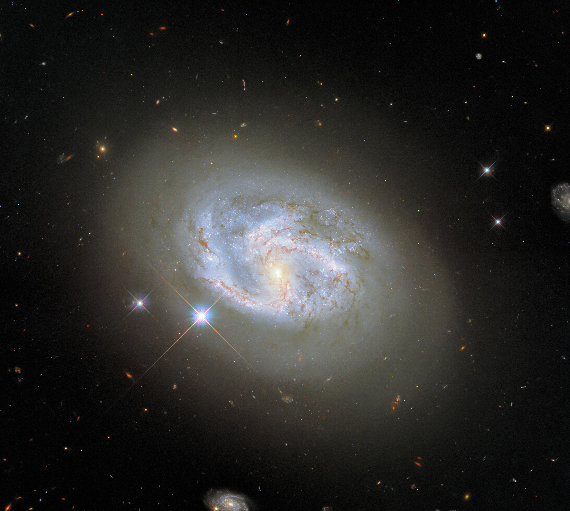 This image, taken with Hubble’s Wide Field Camera 3 (WFC3), features the spiral galaxy NGC 4680. At 2 o’clock and 7 o’clock two other galaxies can be seen flanking NGC 4680. NGC 4680 enjoyed a wave of attention in 1997, as it played host to a supernova explosion known as SN 1997bp. Amazingly, the supernova was identified by an Australian amateur astronomer named Robert Evans, who has identified an extraordinary 42 supernova explosions.   NGC 4680 is actually a rather tricky galaxy to classify. It is sometimes referred to as a spiral galaxy, but it is also sometimes classified as a lenticular galaxy. Lenticular galaxies fall somewhere in between spiral galaxies and elliptical galaxies. Whilst NGC 4680 does have distinguishable spiral arms, they are not clearly defined, and the tip of one arm appears very diffuse. Galaxies are not static, and their morphologies (and therefore their classifications) vary throughout their lifetimes. Spiral galaxies are thought to evolve into elliptical galaxies, most likely by merging with one another, causing them to lose their distinctive spiral structures.  Links Video of A Spiral Amongst Friends Credit:  ESA/Hubble & NASA, A. Riess et al.