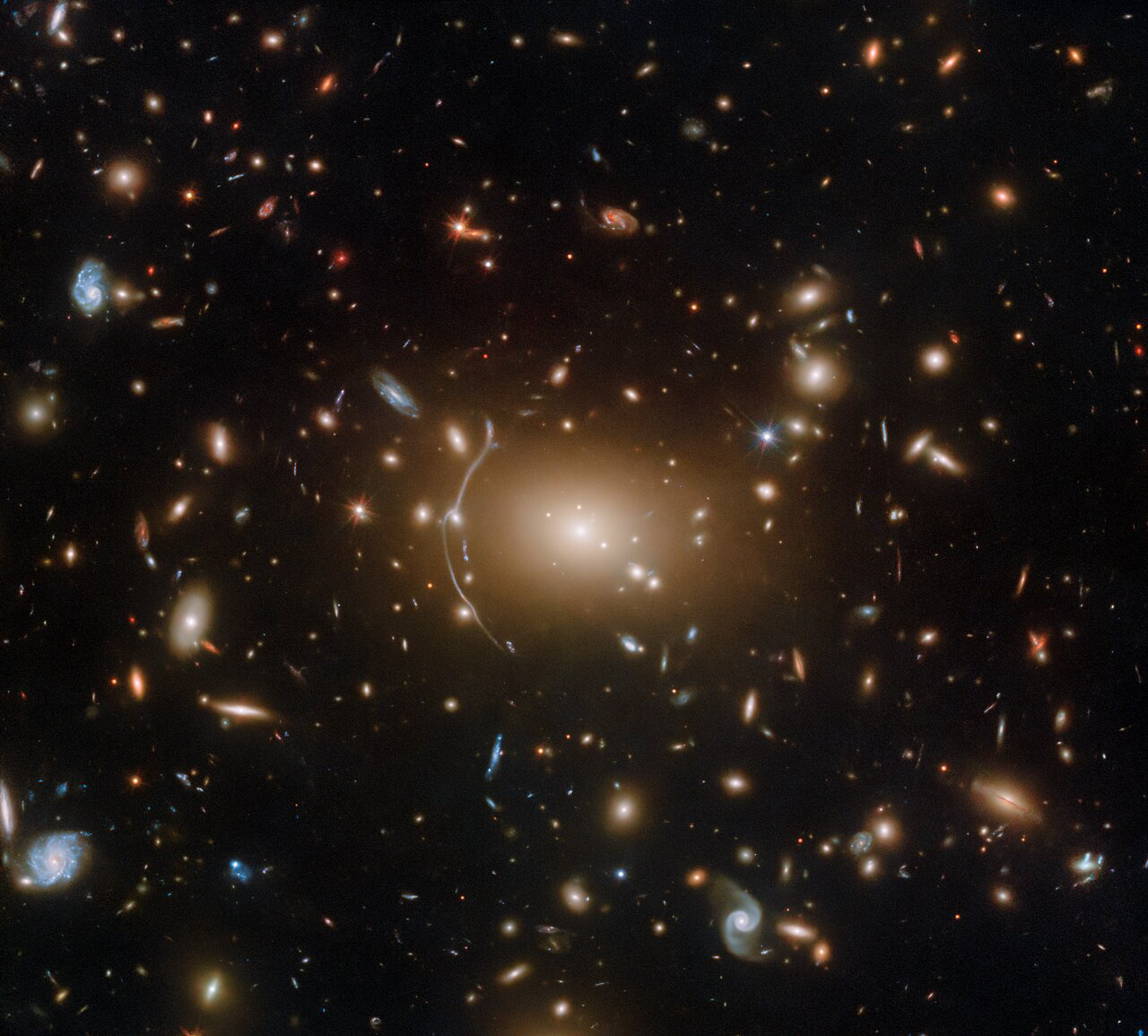 In celebration of Halloween, Hubble brings you this inky image of the galaxy cluster Abell 611, located roughly 3.2 billion light years from Earth.   This object is a popular target for investigating dark matter, in part because of the numerous examples of strong gravitational lensing visible amongst the cluster’s intricate web of galaxies.  [Image Description: Hundreds of small galaxies appear across this view. Their colours vary. Some are shades of orange, while others are white. Most appear as fuzzy ovals, but a few have distinct spiral arms. There are also many thin, long, orange arcs that curve around the centre of the image, where there is a prominent orange glow.]  Credit: ESA/Hubble, NASA, P. Kelly, M. Postman, J. Richard, S. Allen