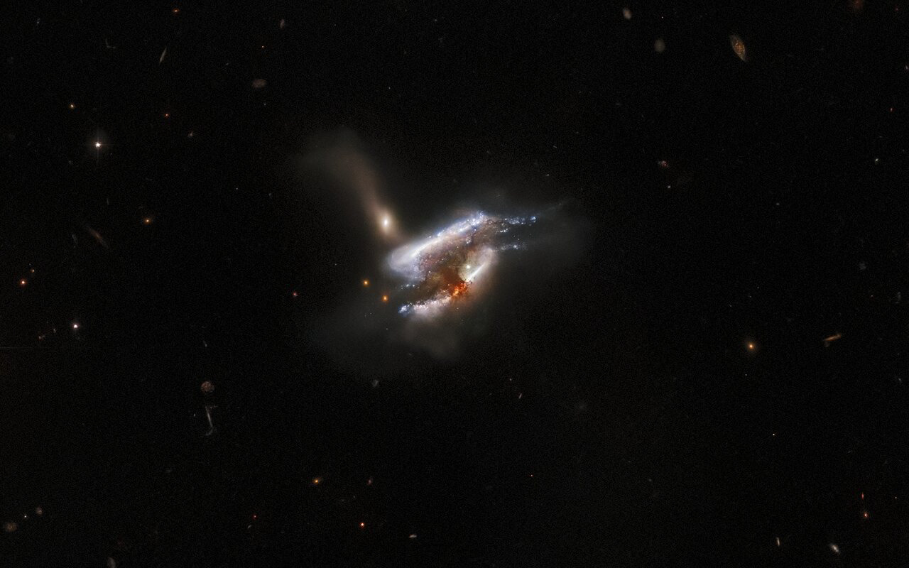 The mass of dust and bright swirls of stars in this image are the distant galaxy merger IC 2431, which lies 681 million light-years from Earth in the constellation Cancer. The NASA/ESA Hubble Space Telescope has captured what appears to be a triple galaxy merger in progress, as well as a tumultuous mixture of star formation and tidal distortions caused by the gravitational interactions of this galactic trio. The centre of this image is obscured by a thick cloud of dust — though light from a background galaxy can be seen piercing its outer extremities.    This image is from a series of Hubble observations investigating weird and wonderful galaxies found by the Galaxy Zoo citizen science project. Using Hubble’s powerful Advanced Camera for Surveys (ACS), astronomers took a closer look at some of the more unusual galaxies that volunteers had identified. The original Galaxy Zoo project was the largest galaxy census ever carried out, and relied on crowdsourcing time from more than 100 000 volunteers to classify 900 000 unexamined galaxies. The project achieved what would have been years of work for a professional astronomer in only 175 days, and has led to a steady stream of similar astronomical citizen science projects. Later Galaxy Zoo projects have included the largest ever studies of galaxy mergers and tidal dwarf galaxies, as well as the discovery of entirely new types of compact star-forming galaxies.  Credit: ESA/Hubble & NASA, W. Keel, Dark Energy Survey, DOE, FNAL, DECam, CTIO, NOIRLab/NSF/AURA, SDSS Acknowledgement: J. Schmidt