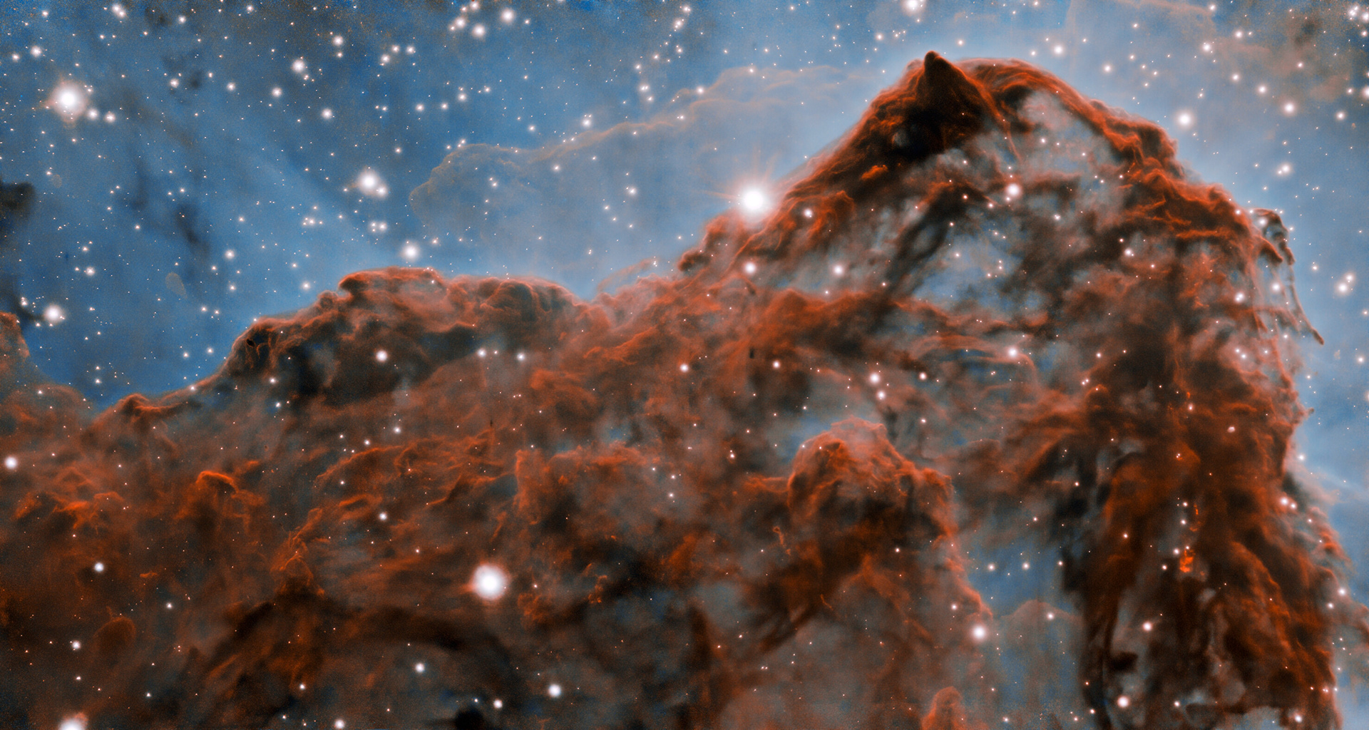 A 50-trillion-km (33-trillion-mile, or 5 light-year) long section of the western wall in the Carina Nebula, as observed with adaptive optics on the Gemini South telescope. This mountainous section of the nebula reveals a number of unusual structures including a long series of parallel ridges that could be produced by a magnetic field, a remarkable almost perfectly smooth wave, and fragments that appear to be in the process of being sheared off the cloud by a strong wind. There is also evidence for a jet of material ejected from a newly-formed star. The exquisite detail seen in the image is in part due to a technology known as adaptive optics, which resulted in a ten-fold improvement in the resolution of the research team’s observations.  Credit: International Gemini Observatory/NOIRLab/NSF/AURA  Acknowledgment:   PI: Patrick Hartigan (Rice University)  Image processing: Patrick Hartigan (Rice University), Travis Rector (University of Alaska Anchorage), Mahdi Zamani & Davide de Martin