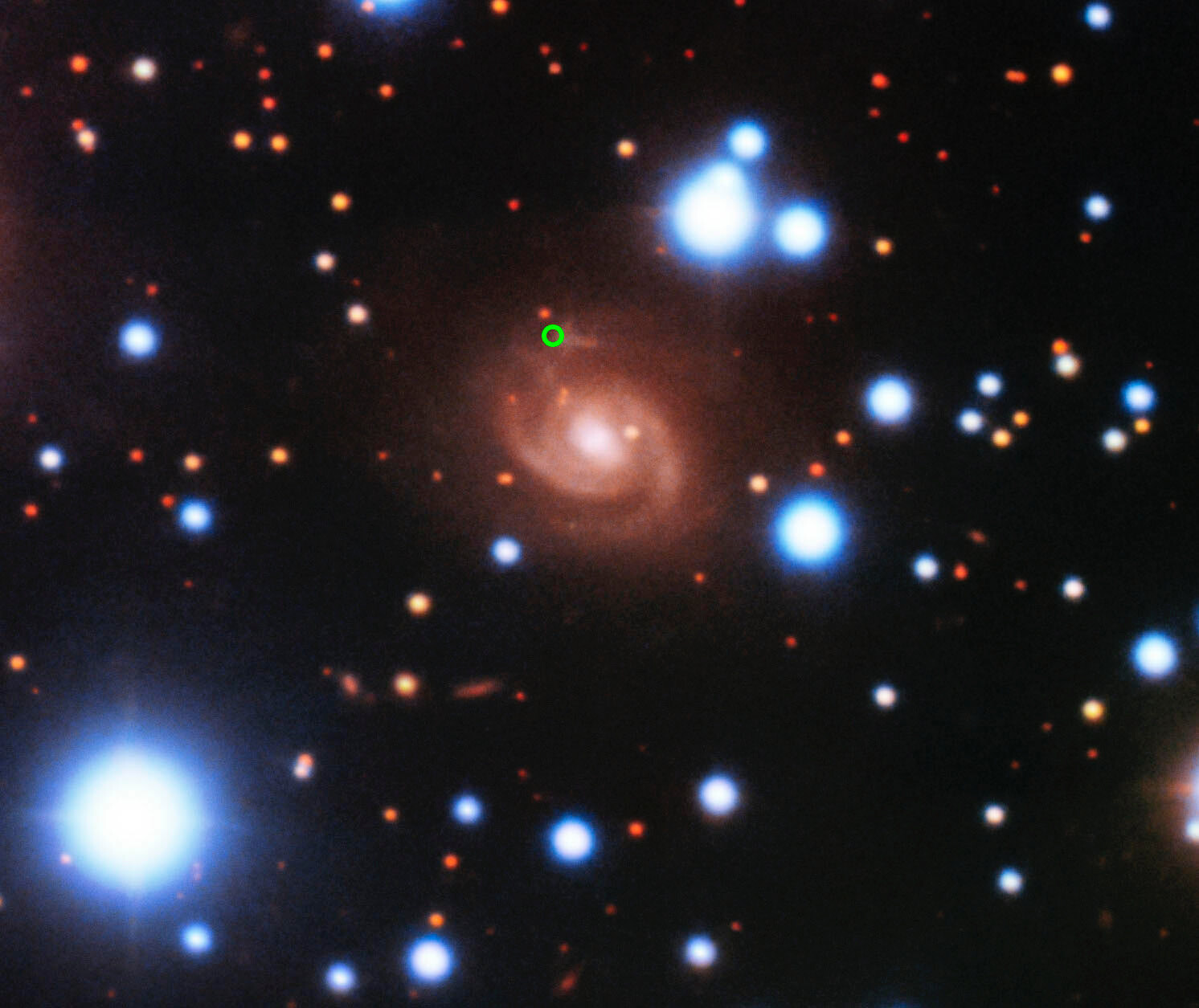 Fast Radio Burst 180916 Host Galaxy (annotated) Image of the host galaxy of FRB 180916 (center) acquired with the 8-meter Gemini-North telescope of NOIRLab on Hawaii’s Maunakea. Images acquired in SDSS g’, r’, and z’ filters are used for the blue, green, and red colors, respectively. The position of the FRB in the spiral arm of the galaxy is marked by a green circle.  Credit: Gemini Observatory/NSF’s National Optical-Infrared Astronomy Research Laboratory/AURA