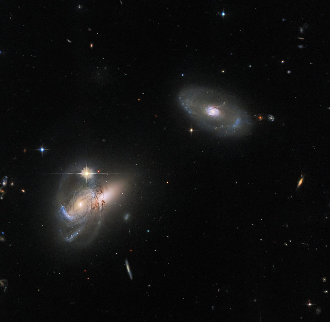 This luminescent image features multiple galaxies, perhaps most noticeably LEDA 58109, the lone galaxy in the upper right. LEDA 58109 is flanked by two further galactic objects to its lower left — an active galactic nucleus (AGN) called SDSS J162558.14+435746.4 that partially obscures the galaxy SDSS J162557.25+435743.5, which appears to poke out to the right behind the AGN.   Galaxy classification is sometimes presented as something of a dichotomy: spiral and elliptical. However, the diversity of galaxies in this image alone highlights the complex web of galaxy classifications that exist, including galaxies that house extremely luminous AGNs at their cores, and galaxies whose shapes defy the classification of either spiral or elliptical.   The sample of galaxies here also illustrates the wide variety of names that galaxies have: some relatively short, like LEDA 58109, and some very long and challenging to remember, such as the two galaxies to the left. This is due to the variety of cataloguing systems that chart the celestial objects in the night sky. No one catalogue is exhaustive, and they cover overlapping regions of the sky, so that many galaxies belong to several different catalogues. For example, the galaxy on the right is LEDA 58109 in the LEDA galaxy database, but is also known as MCG+07-34-030 in the MCG galaxy catalogue, and SDSS J162551.50+435747.5 in the SDSS galaxy catalogue — the same catalogue that also lists the two galaxies to the left.  Links Video of Follow the LEDA Credit: ESA/Hubble & NASA, W. Keel