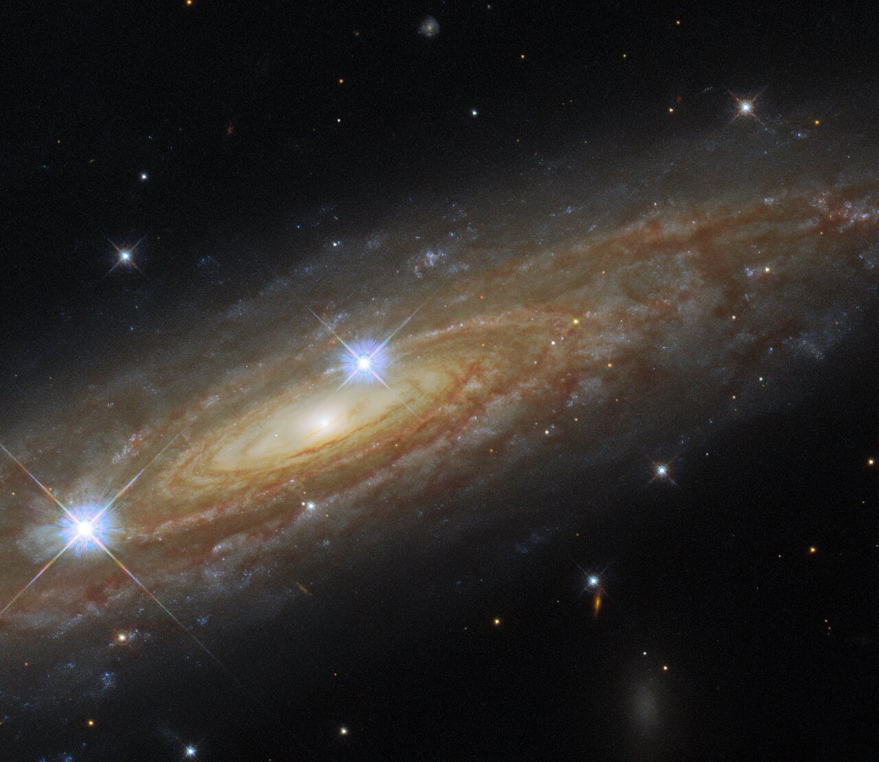 This astronomical portrait from the NASA/ESA Hubble Space Telescope showcases an edge-on view of the majestic spiral galaxy UGC 11537. Hubble’s Wide Field Camera 3 has captured the tightly wound spiral arms swirling around the heart of UGC 11537 at infrared and visible wavelengths, showing both the bright bands of stars and the dark clouds of dust threading throughout the galaxy.   UGC 11537 is 230 million light-years away in the constellation Aquila, and lies close to the plane of the Milky Way. Being so close to the starry band of the Milky Way means that foreground stars from our own galaxy have crept into the image — the two prominent stars in front of UGC 11537 are interlopers from within the Milky Way. These bright foreground stars are surrounded by diffraction spikes — imaging artifacts caused by starlight interacting with Hubble’s inner structure.   This image came from a set of observations designed to help astronomers weigh supermassive black holes in distant galaxies. The combination of Hubble’s sharp-eyed observations and data from ground-based telescopes allowed astronomers to make detailed models of the mass of stars in these galaxies, which in turn helps constrain the mass of supermassive black holes.  Links Video of A Spectacular Side-On Spiral Credit: ESA/Hubble & NASA, A. Seth