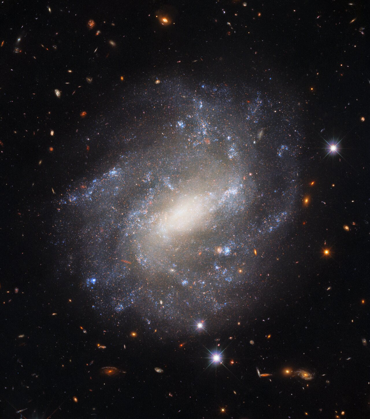 The lonely spiral galaxy UGC 9391 is shown in this image from the NASA/ESA Hubble Space Telescope’s Wide Field Camera 3. This galaxy resides 130 million light-years from Earth in the constellation Draco near the north celestial pole. The star-studded spiral arms stand in splendid isolation against a backdrop of distant galaxies, which are only visible as indistinct swirls or smudges thanks to their vast distances from Earth. The image also features some much brighter foreground stars closer to home. These bright nearby stars are ringed with diffraction spikes — prominent spikes caused by light interacting with the inner workings of Hubble’s complicated optics.   This image is from a set of Hubble observations which astronomers used to construct the “Cosmic Distance Ladder” — a set of connected measurements allowing the distances to the most distant astronomical objects to be determined. Astronomical distances are only directly measurable for relatively nearby objects — closer than 3000 light-years or so. For distances beyond this, astronomers rely on a set of measured correlations calibrated against nearby objects. UGC 9391 helped astronomers improve their distance estimates by providing a natural laboratory in which to compare two measuring techniques — supernova explosions and Cepheid variables. Improving the precision of distance measurements helps astronomers quantify how quickly the Universe is expanding — one of Hubble’s key science goals.   Credit: ESA/Hubble & NASA, A. Riess et al.