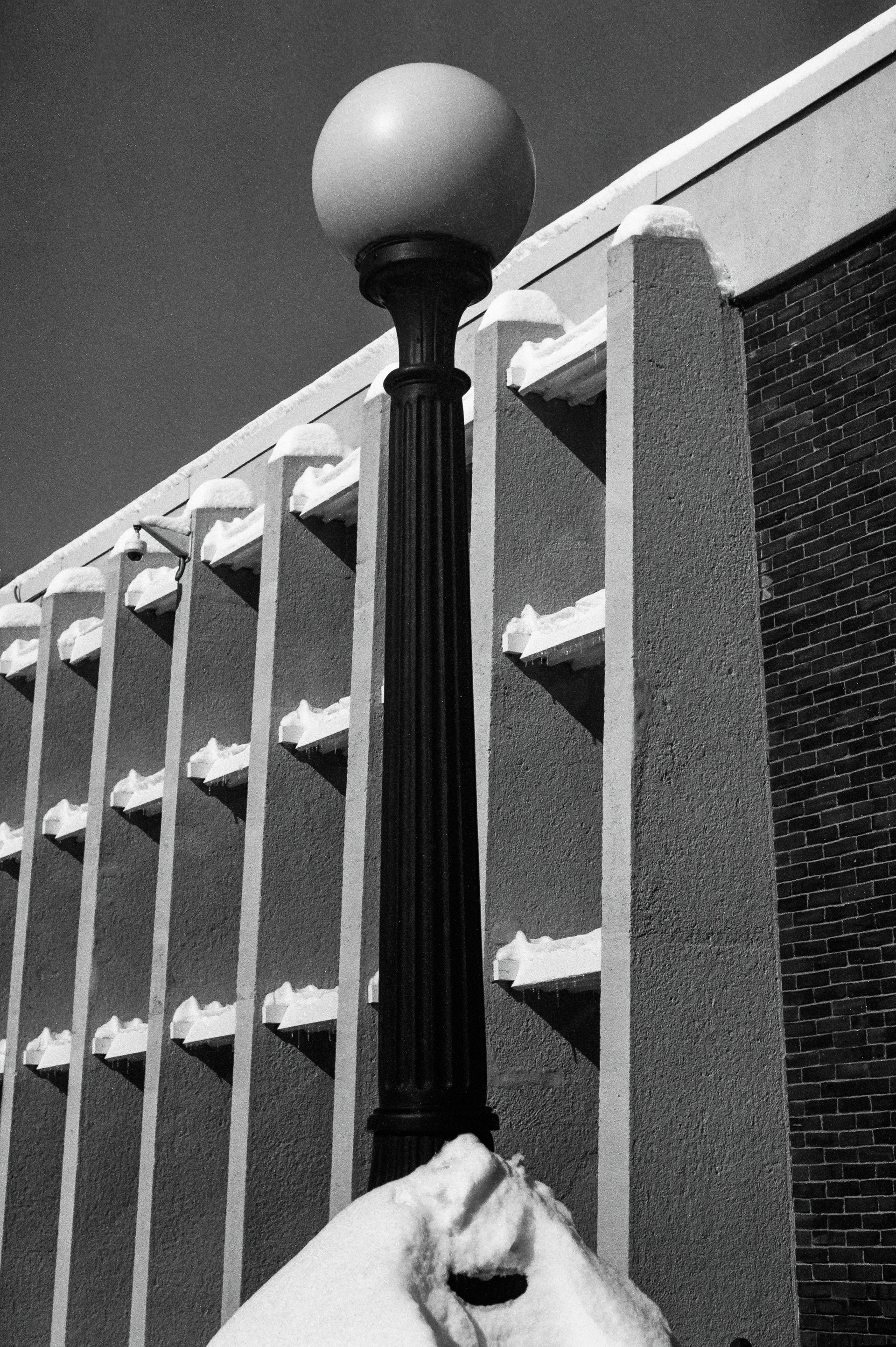 A street light in front of a modern wall after a snowstorm.
