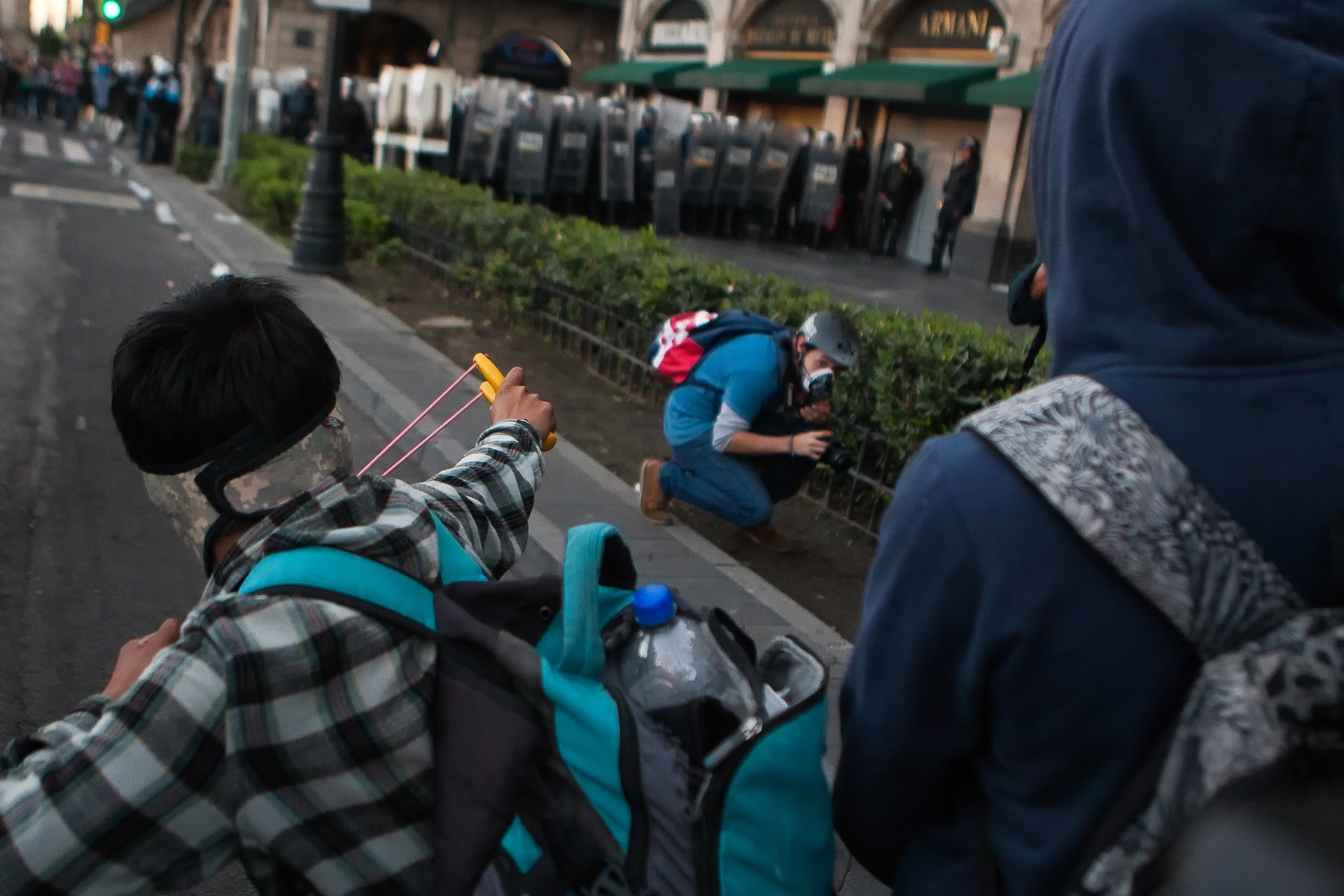 Un manifestante apunta su resortera a una línea de policías del Distrito Federal, mientras un periodista en medio busca cubrirse, el 2 de octubre de 2015. (Foto: Prometeo Lucero)