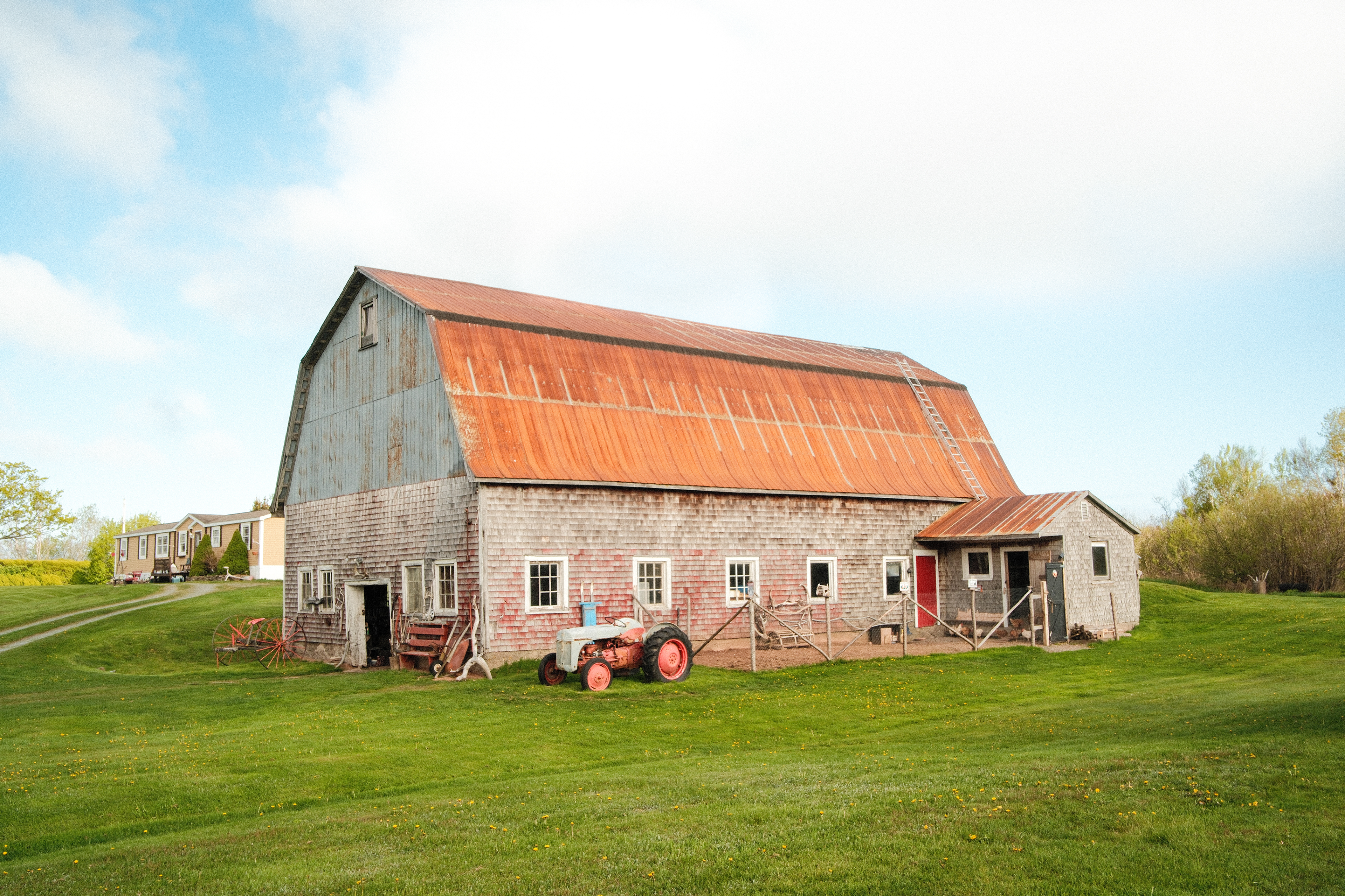 Vieille grange au toit rouge, ciel bleu, vieux tracteur à l'entrée 