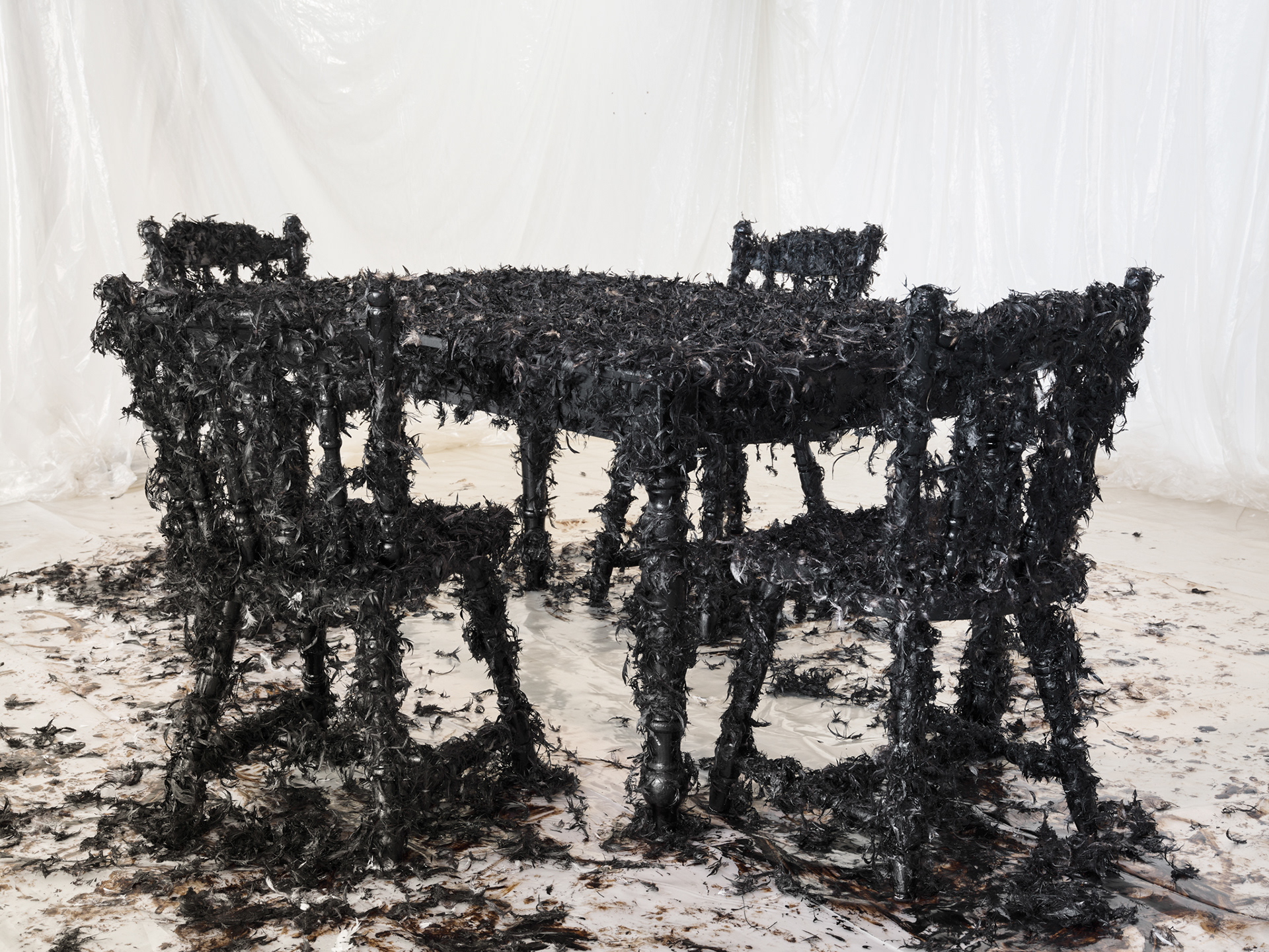 Art installation: Bitumen paint, pillow feathers, recycled wood table and chairs, plastic sheeting. Music 'Welcome to my world' written by Ray Winkler and John Hathcock and performed by Jim Reeves 1962. Installation at Brighton Centre for Contemporary Art, Brighton, UK, 2023.