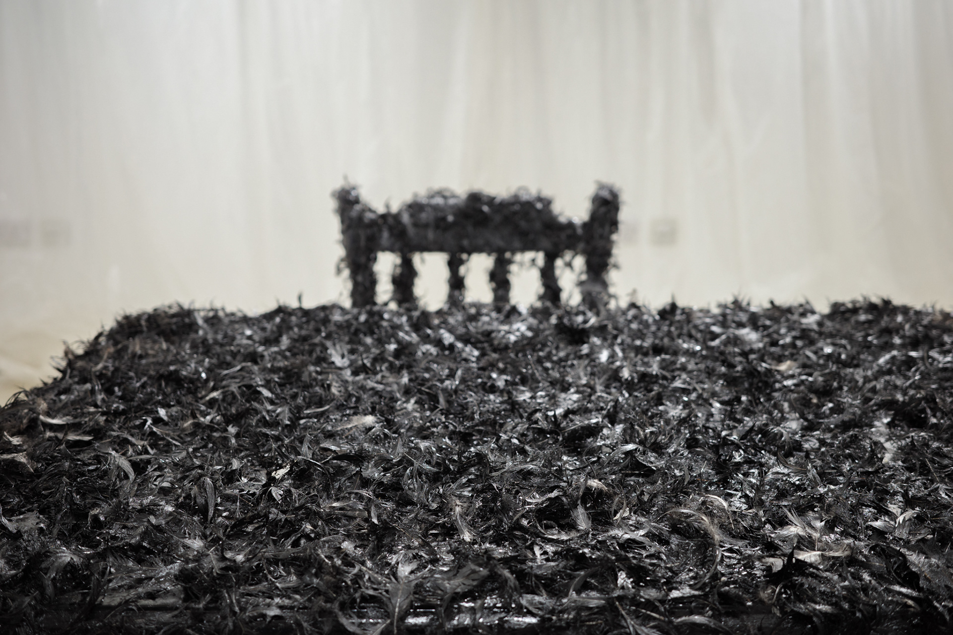 Art installation: Bitumen paint, pillow feathers, recycled wood table and chairs, plastic sheeting. Music 'Welcome to my world' written by Ray Winkler and John Hathcock and performed by Jim Reeves 1962. Installation at Brighton Centre for Contemporary Art, Brighton, UK, 2023.