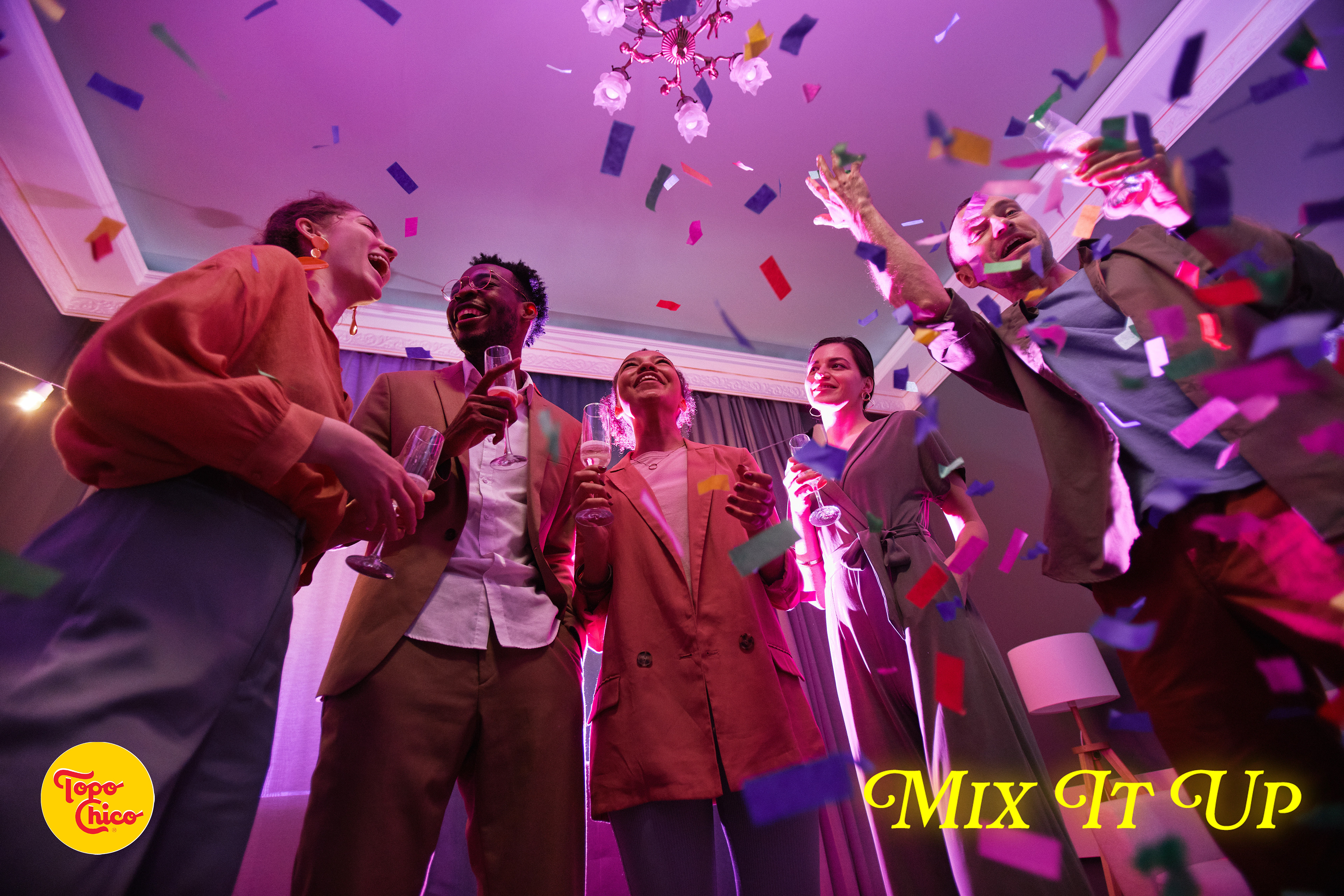 Low angle view at group of young people standing under confetti shower while enjoying party with friends indoors.