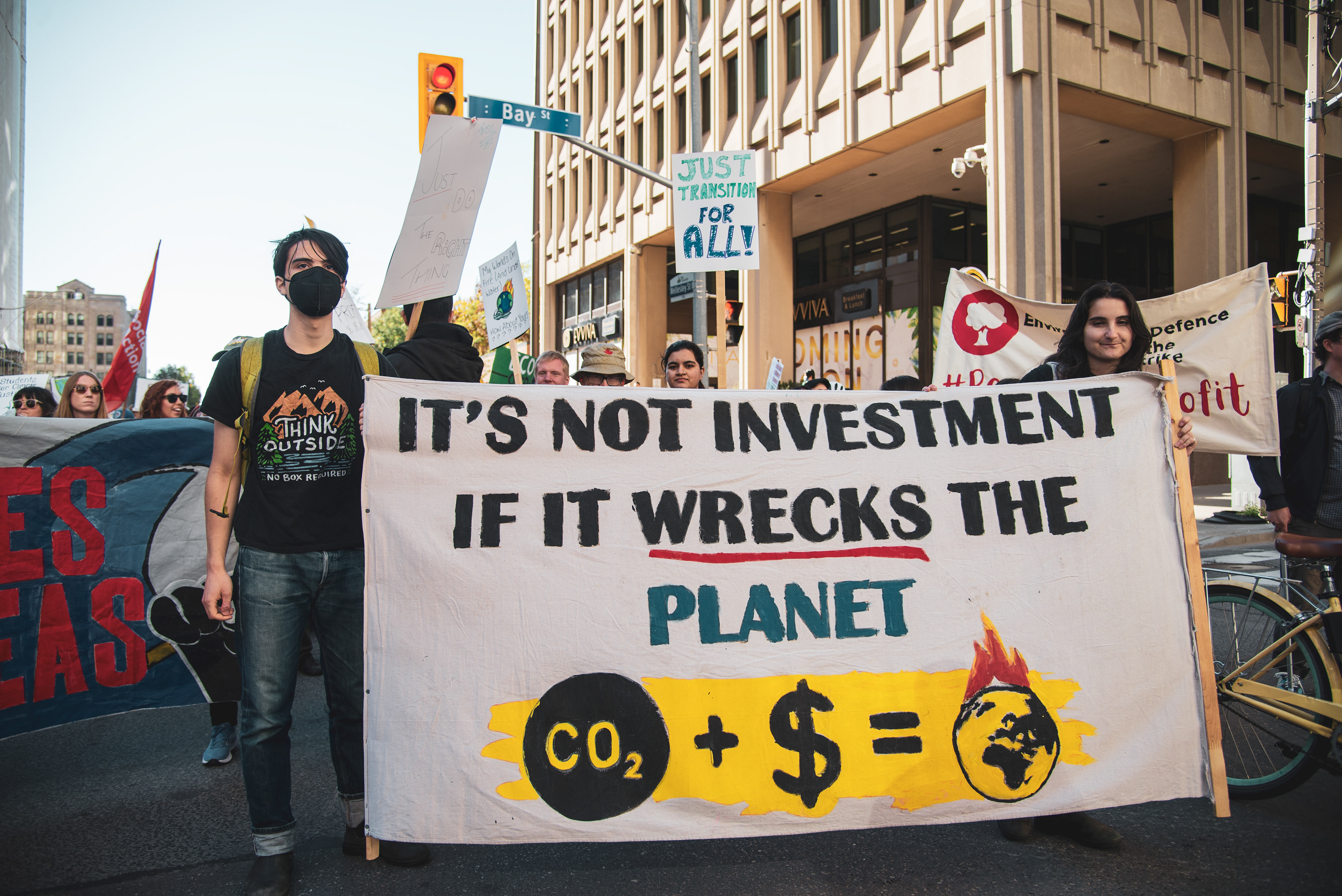 At the corner of Bay and Wellesley Sts., two protesters hold a sign against investment that "wrecks the planet."